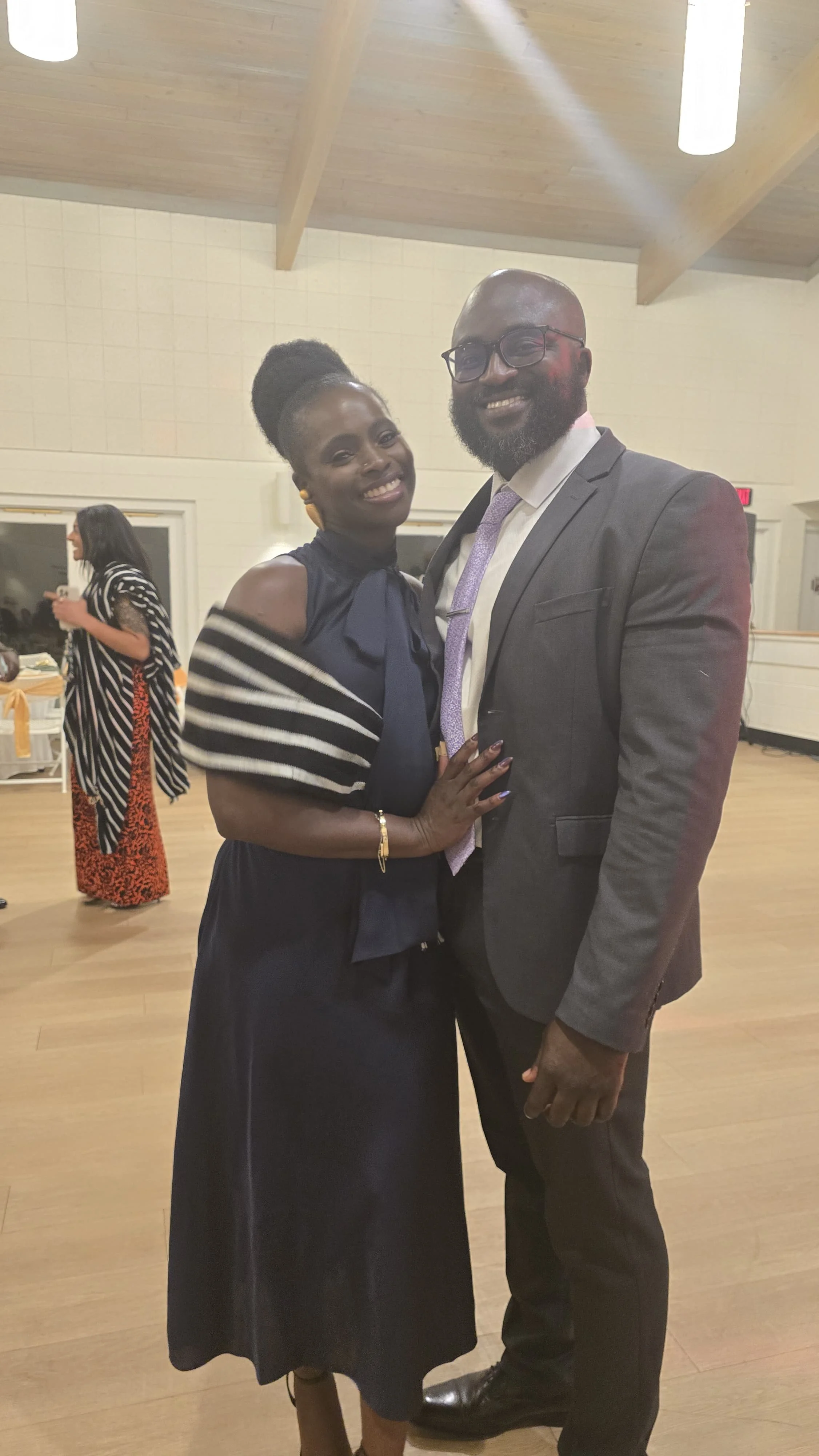 Moyo and Liam dressed in formal attire, posing together at an indoor event. 