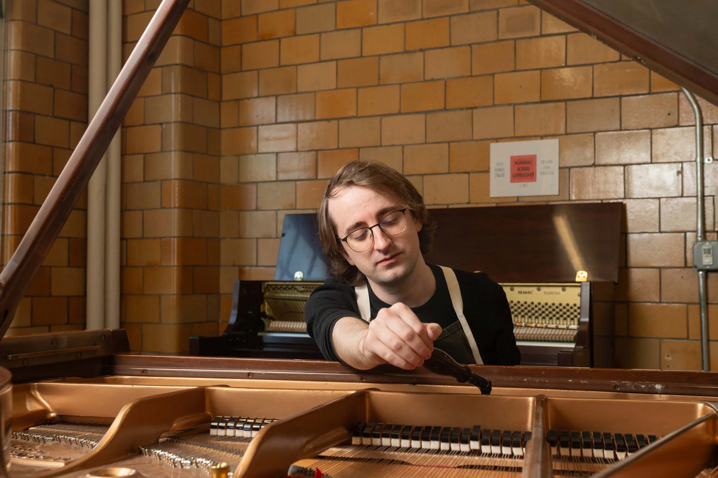 Orlin Twig, A young man with glasses and long brown hair, concentrating on tuning a grand piano.