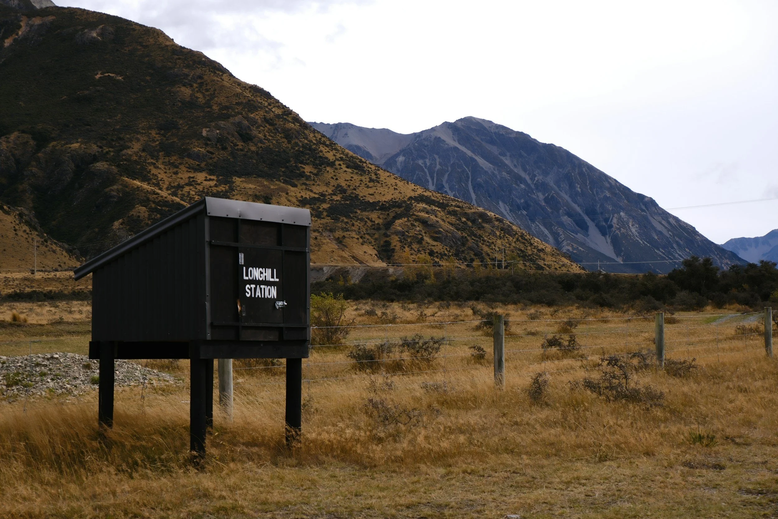 A landscape with mountains in the background and a sign that reads 'Longhill Station' in the foreground.