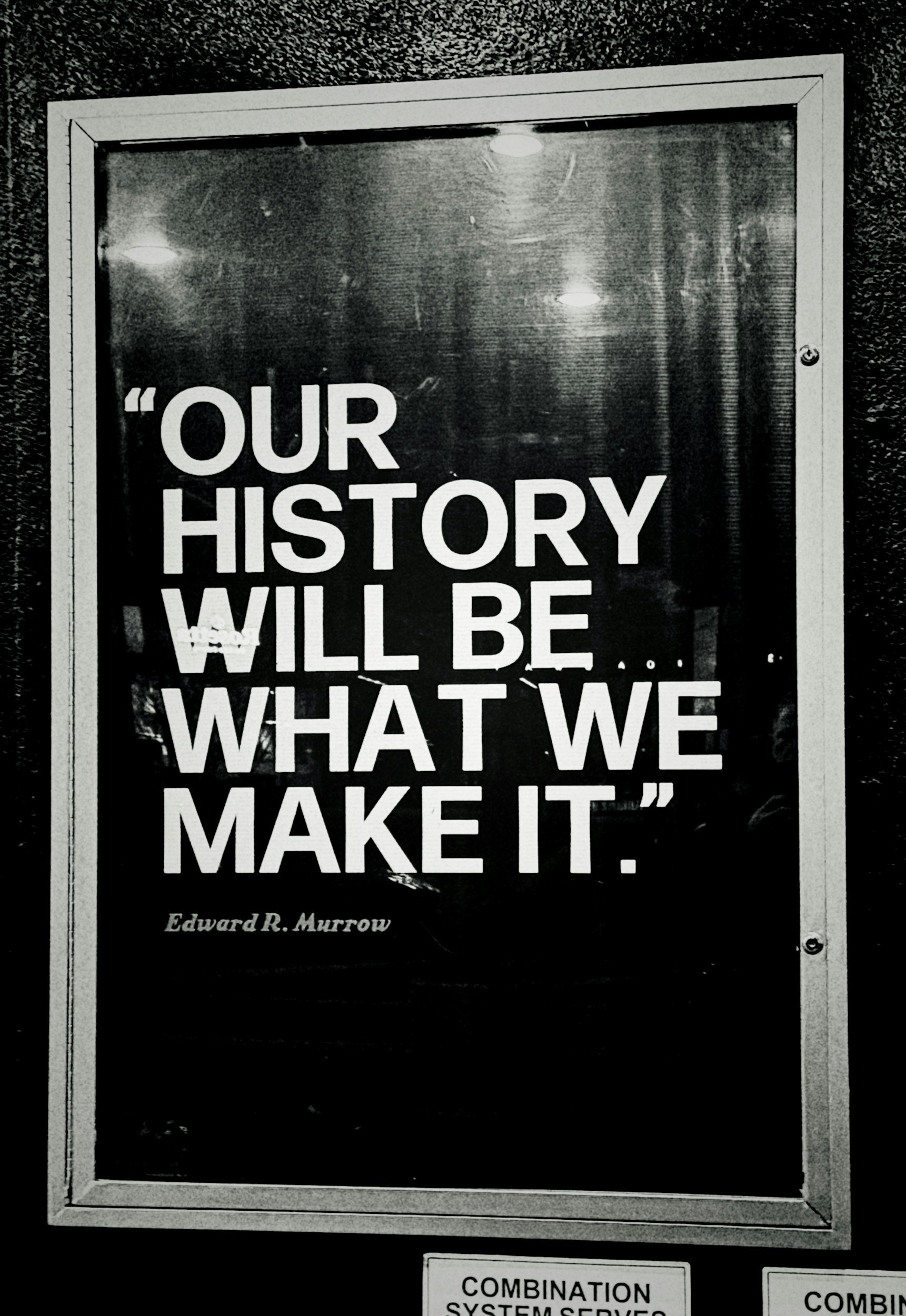 Black and white photo of a sign with the quote 'Our history will be what we make it' by Edward R. Murrow, encased in a window display.