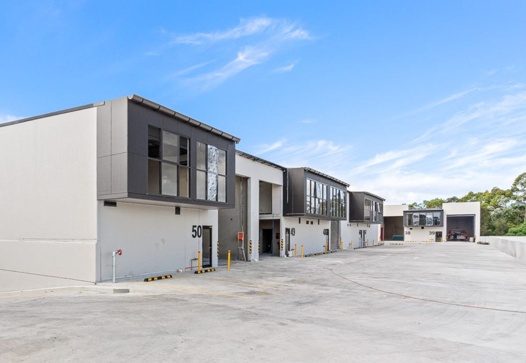 Modern multi-unit residential building with parking lot, numbered units 50, 49, 38, 39, and a garage with a car inside, under a blue sky with a few clouds.