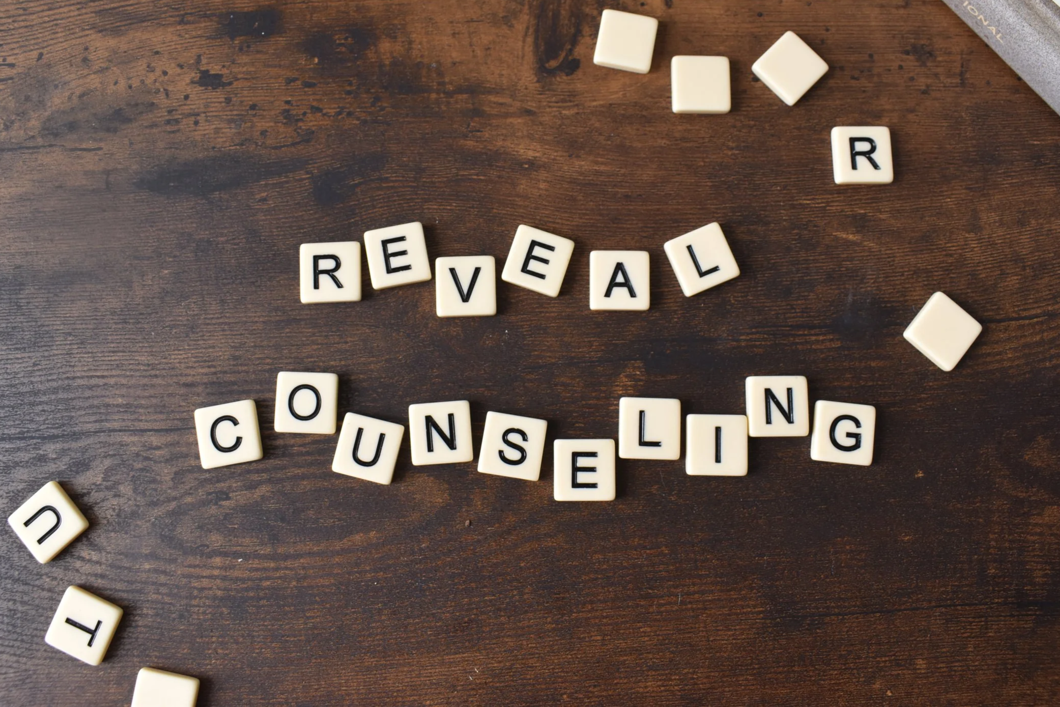Scrabble tiles arranged to spell the words 'REVEAL' and 'CONSEILING' on a wooden surface.