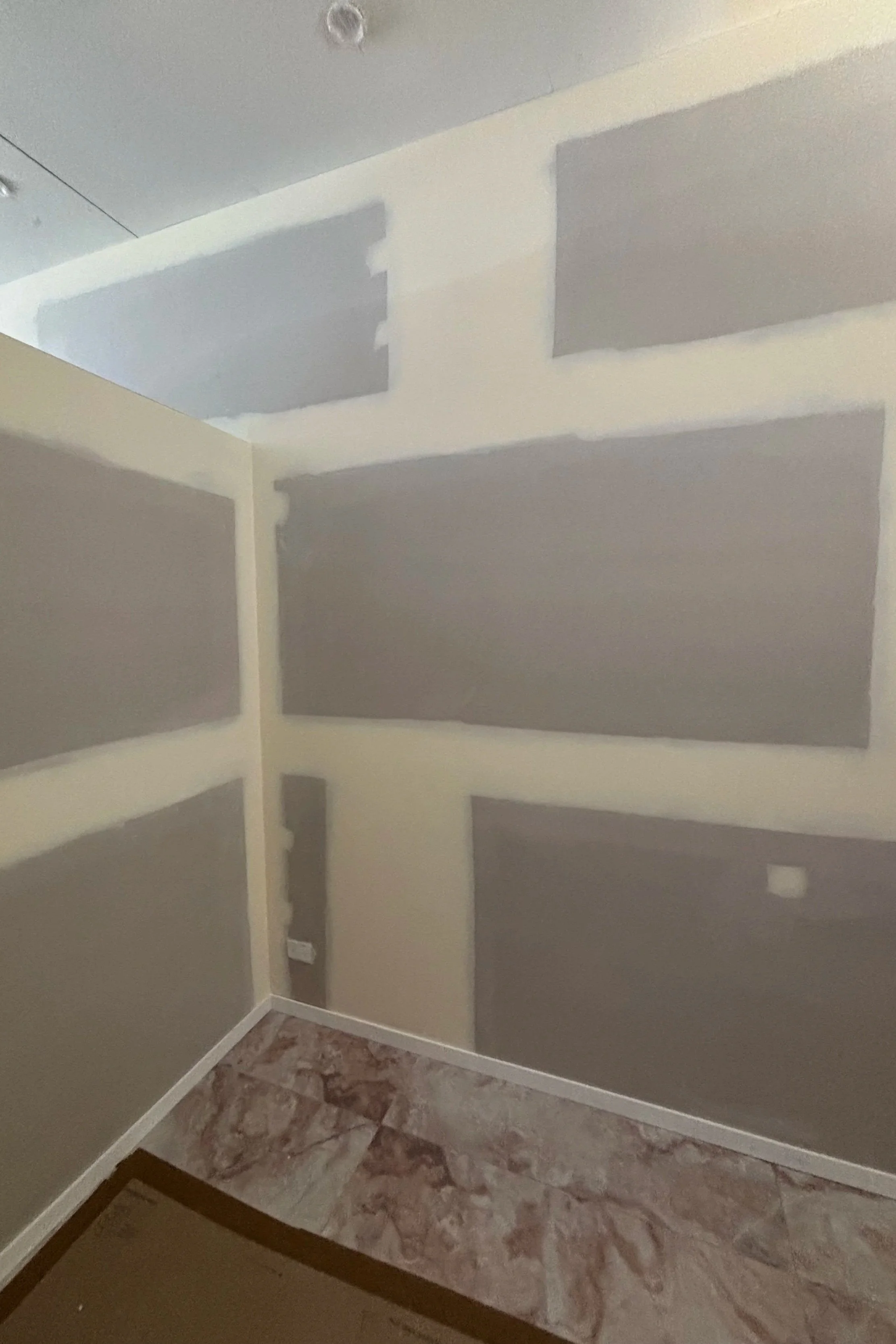 Interior of a room in the process of being painted, with drywall patches visible and no furnishings.