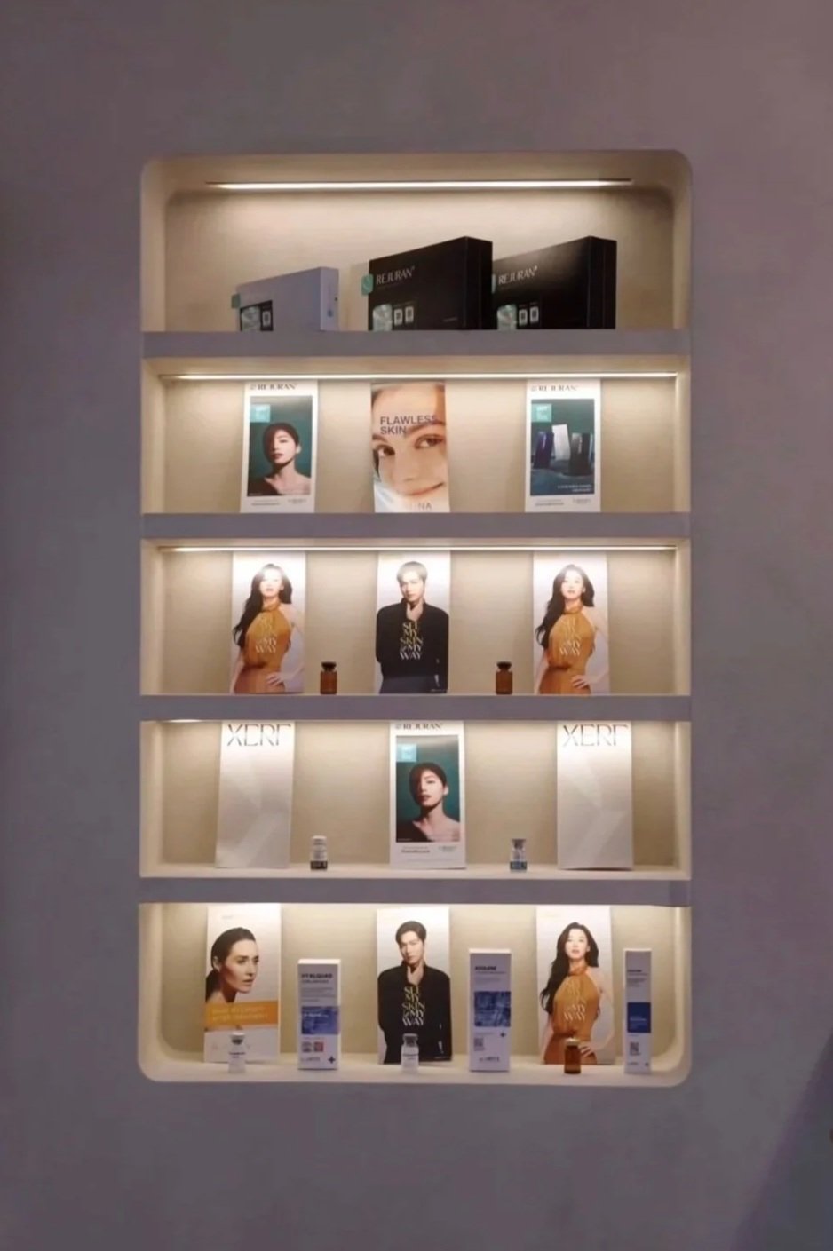 Display shelf with skincare and beauty products, promotional posters of models, and branded packaging in a retail store.