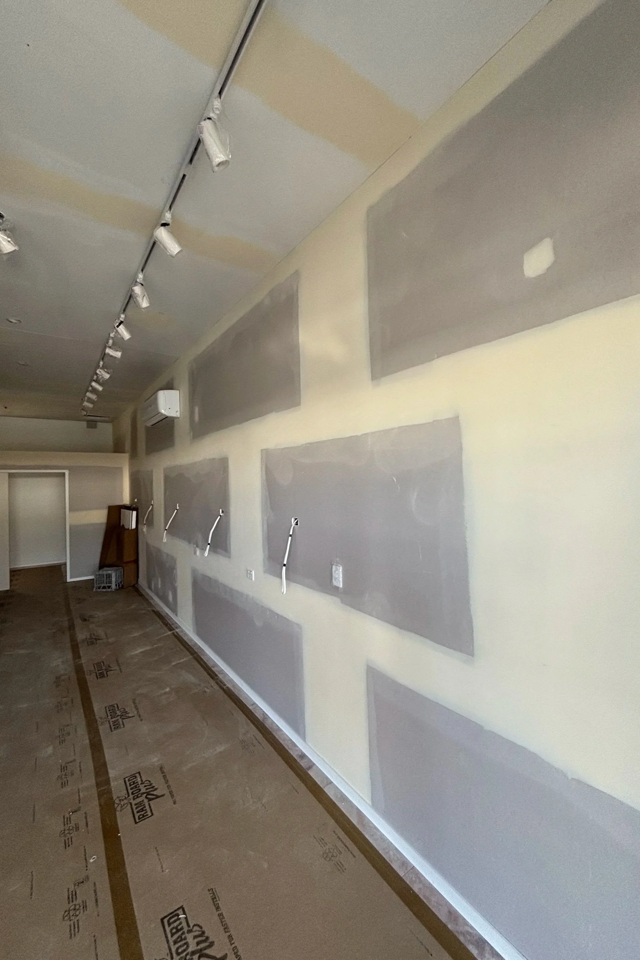 Interior room with unfinished drywall on walls and ceiling, track lighting installed, and a floor covered with protective paper.