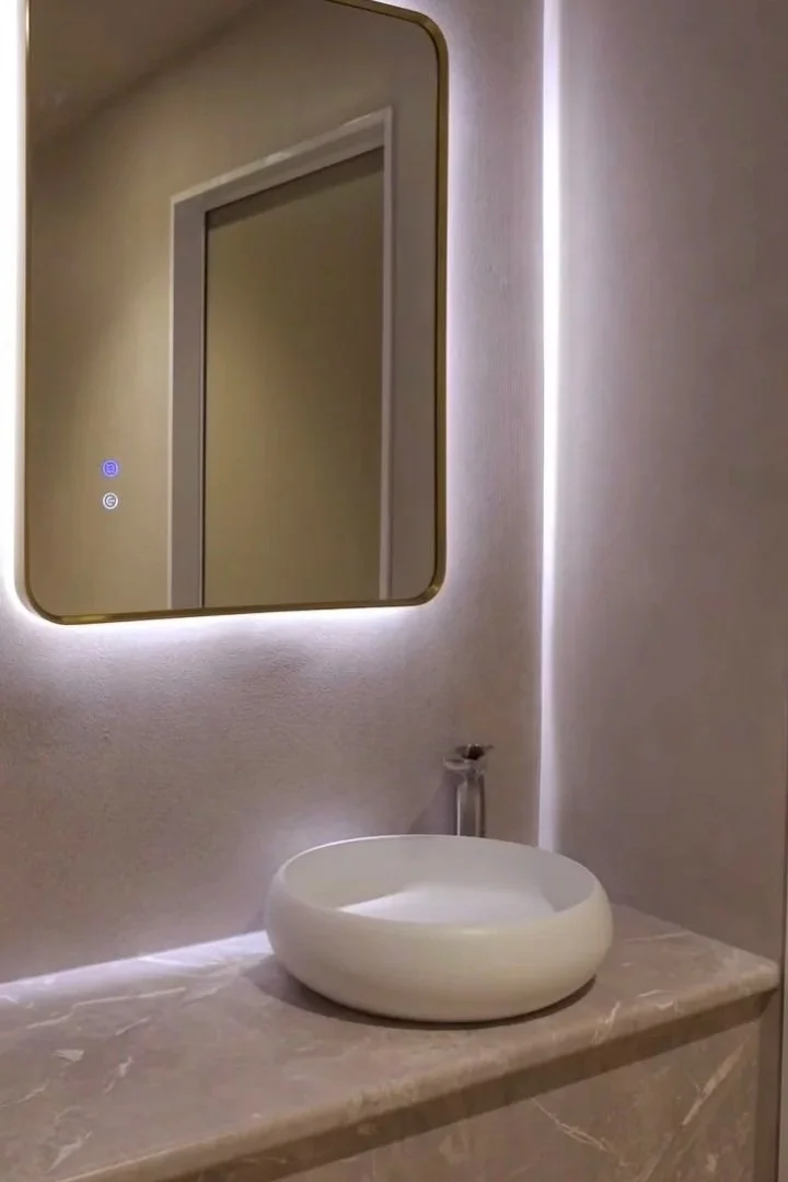 Bathroom with a round vessel sink on a marble countertop, a rectangular mirror with a backlit frame, and a light gray wall.