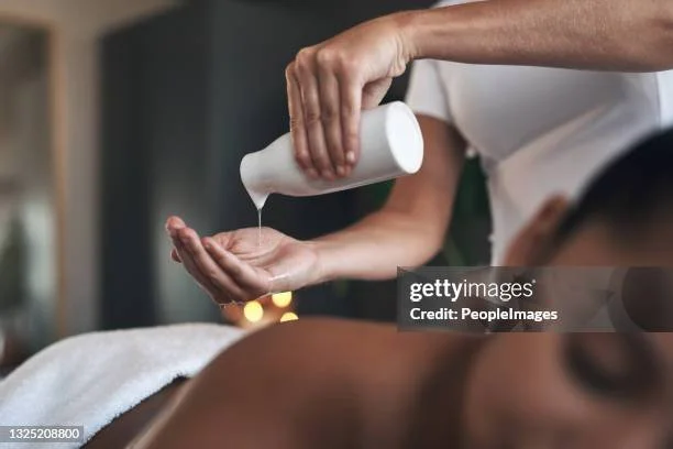 Une personne verse de l'huile ou une lotion sur le dos d'une autre personne allongée, probablement lors d'un soin de massage ou de relaxation.
