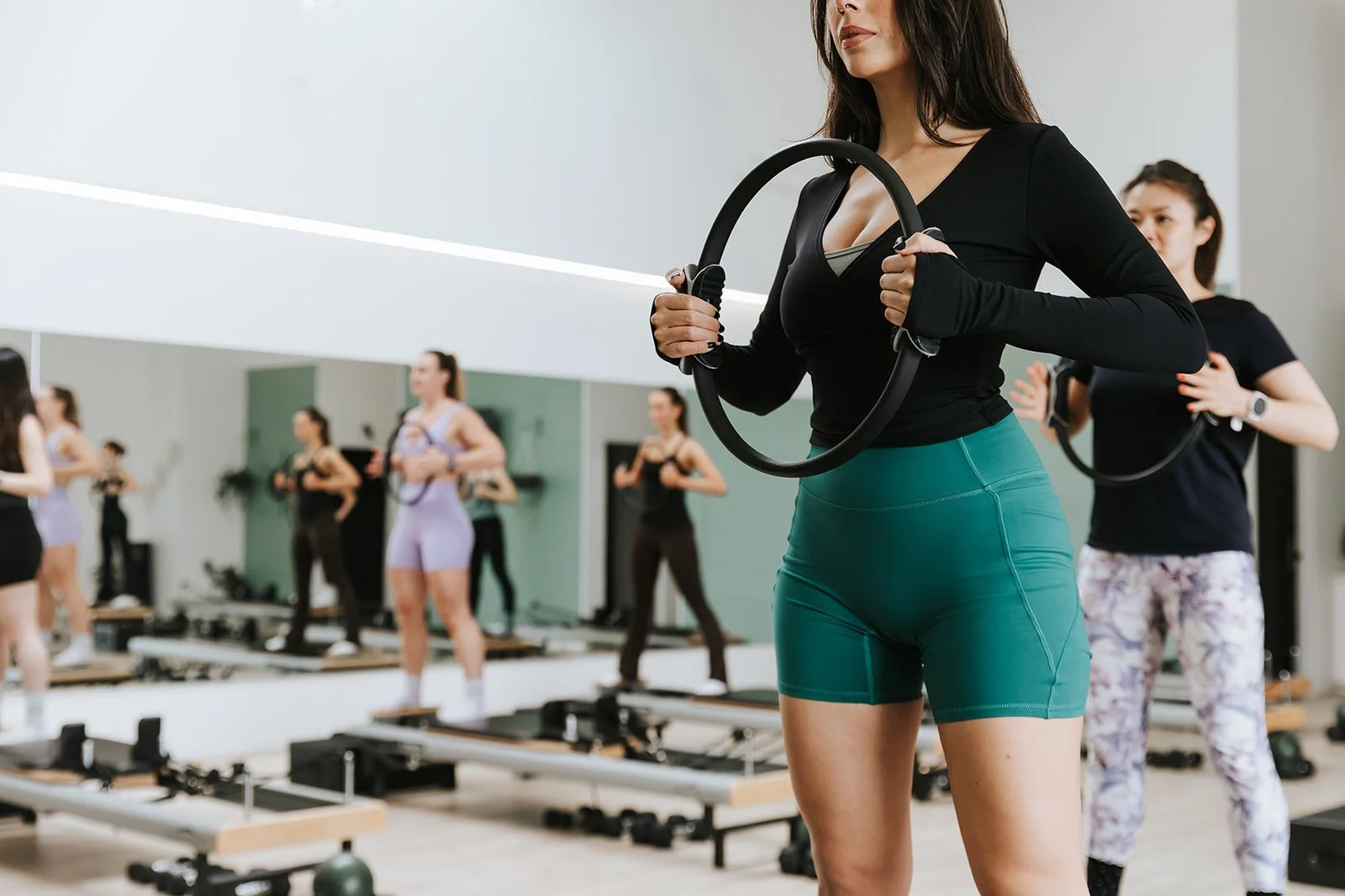Sage Pilates Brunswick West © | Women participating in a fitness class using Pilates rings in a gym, with other women exercising in the background.