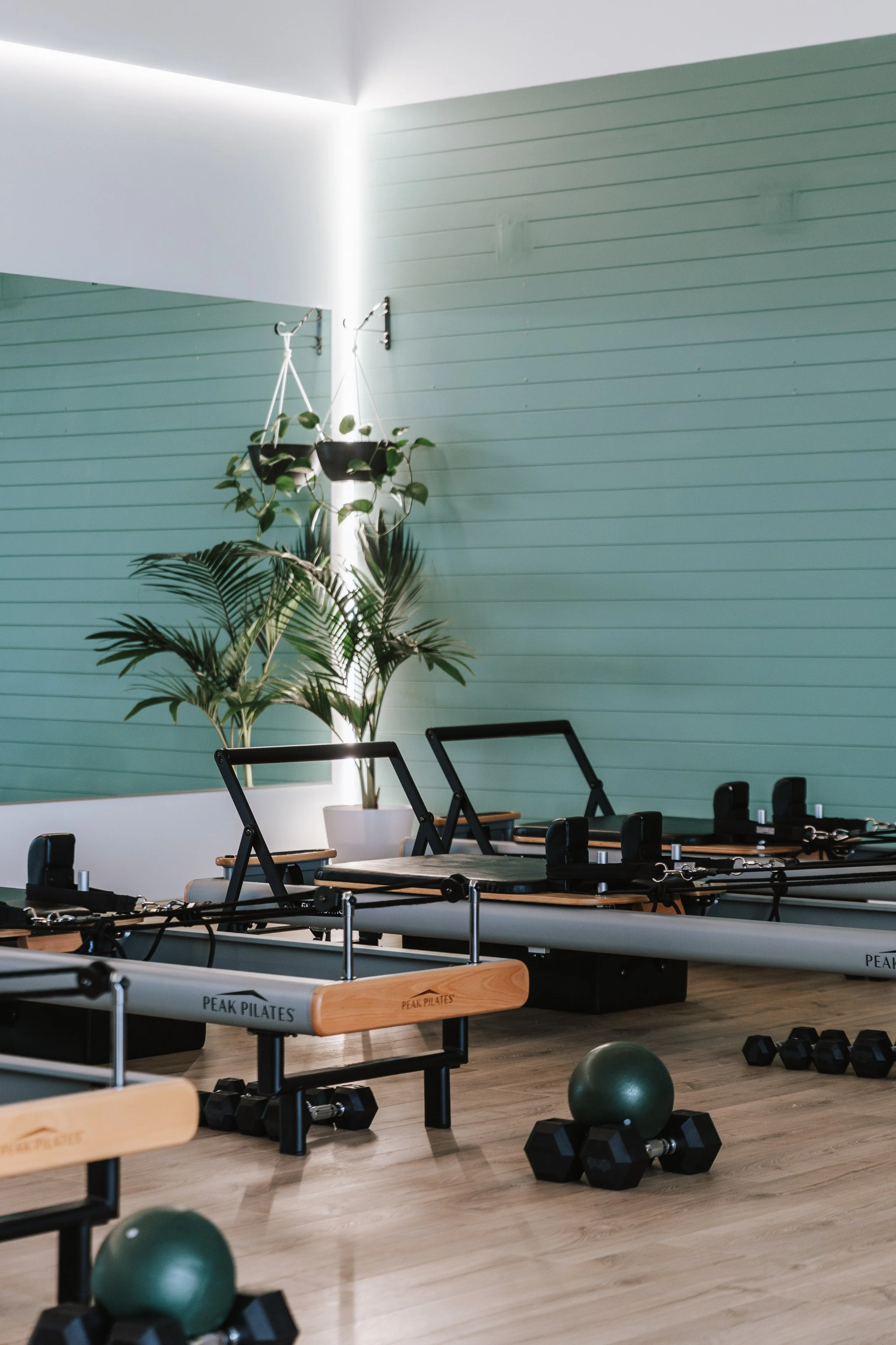 Sage Pilates Brunswick West © | A modern Pilates studio with wooden reformer machines, a large green exercise ball, and dumbbells on a light wooden floor.