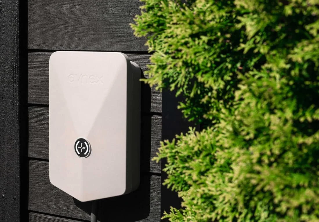 Electrical box mounted on a black wooden wall next to green shrubbery.