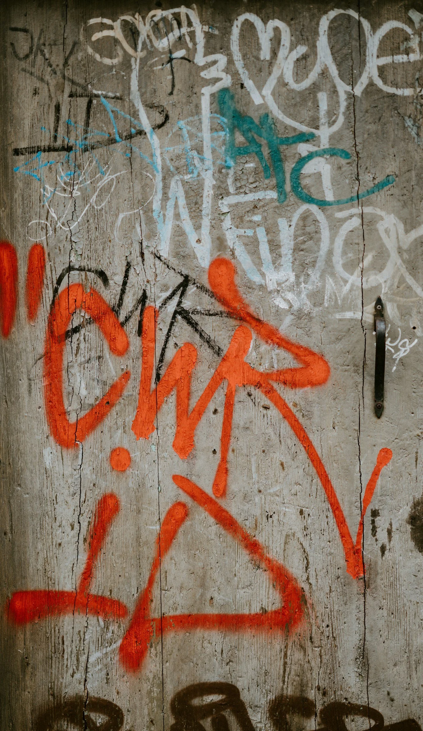 A worn wooden surface covered in various colorful spray paint graffiti and tags, with a black metal latch on the right side.