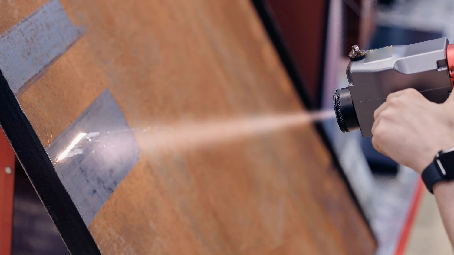 Person using a handheld welding tool on a metal surface, creating sparks and bright light.