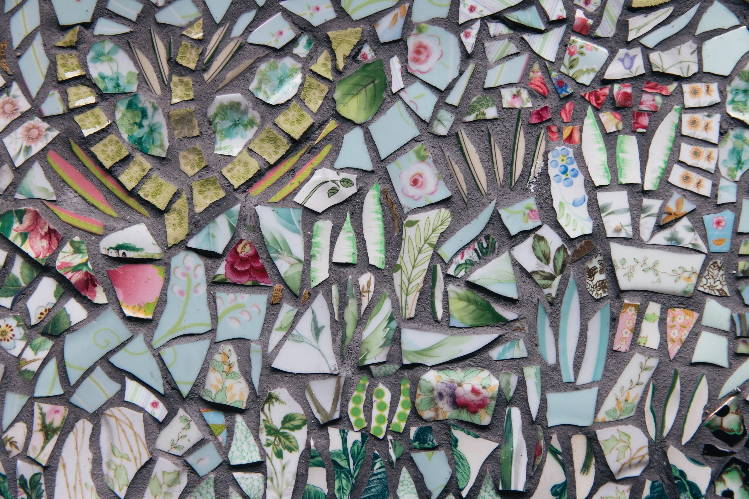 A mosaic made of broken pieces of porcelain with floral and striped patterns in various colors, set on a gray background.