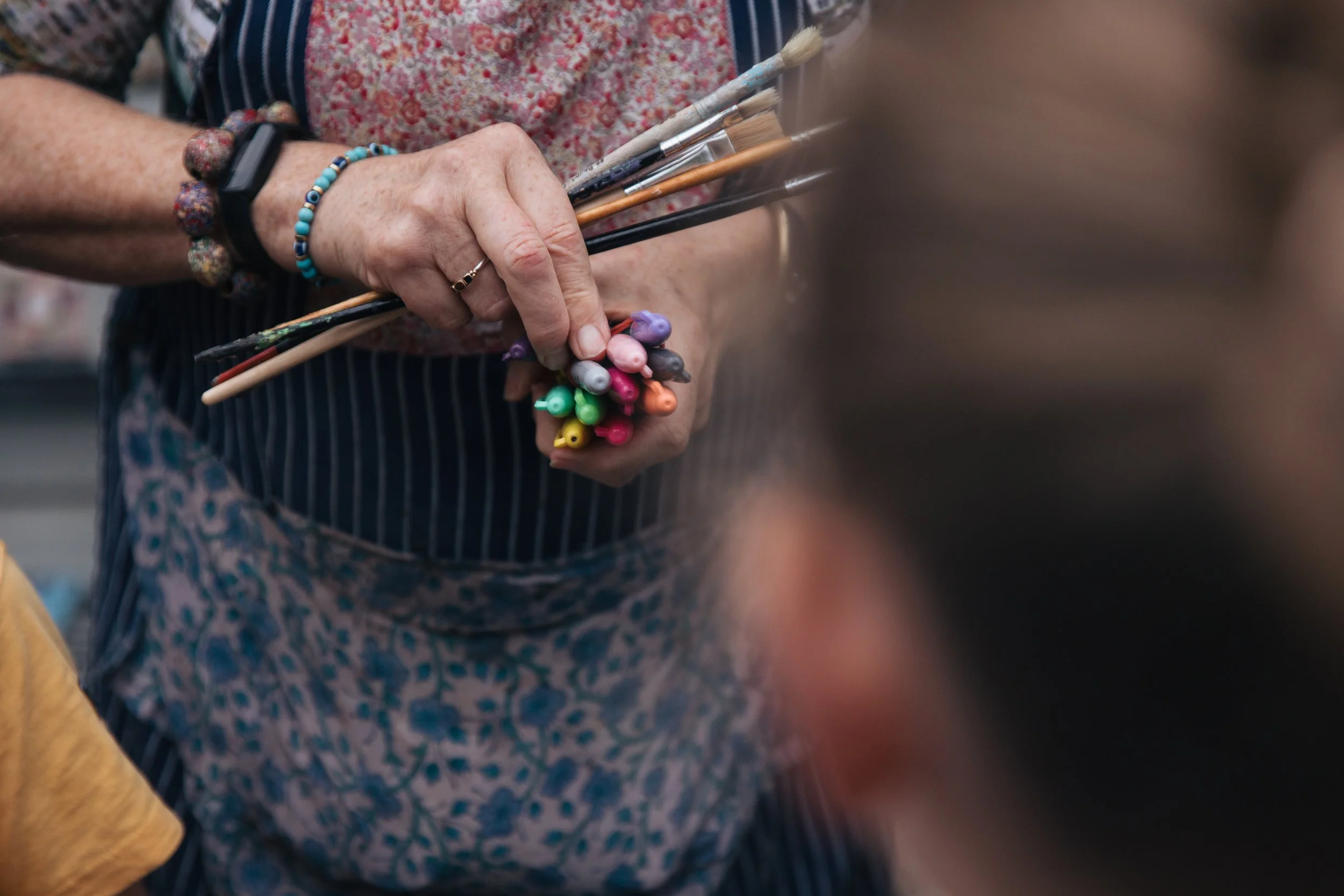 A person holding a bundle of paintbrushes with colorful tips.