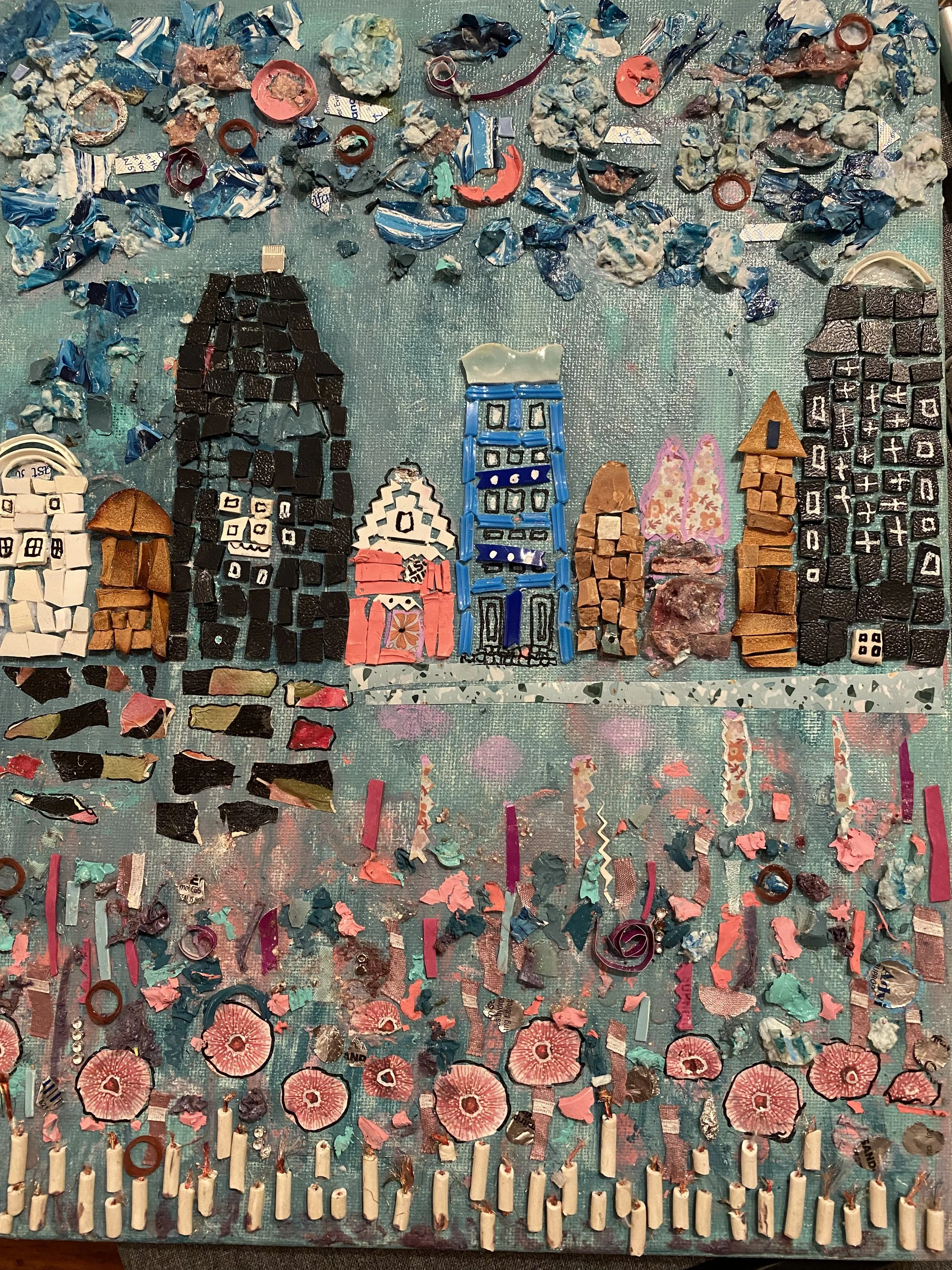 A mosaic art piece created with various pieces of torn paper, buttons, and small objects arranged to depict a cityscape with buildings and a skyline.