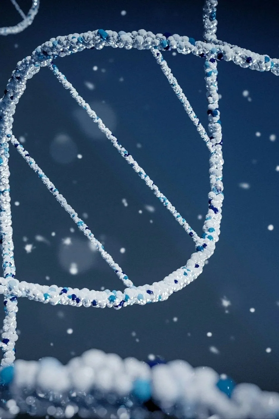 Close-up of a glittering beaded structure in the shape of a globe against a dark blue background with snowflakes falling.