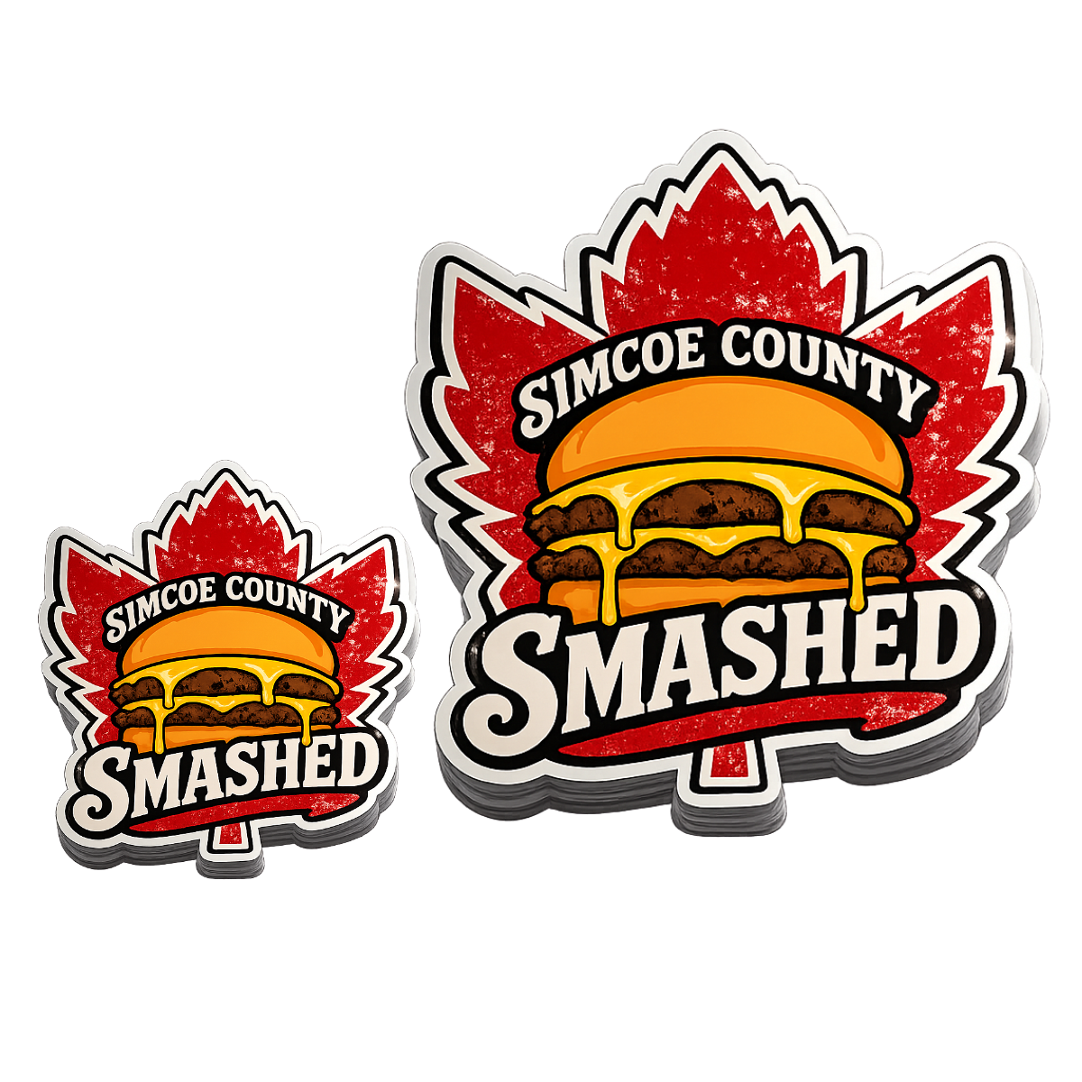 Brightly colored stickers with a maple leaf background, featuring a cheeseburger with cheese dripping over the sides, and text reading 'Simcoe County Smashed'.