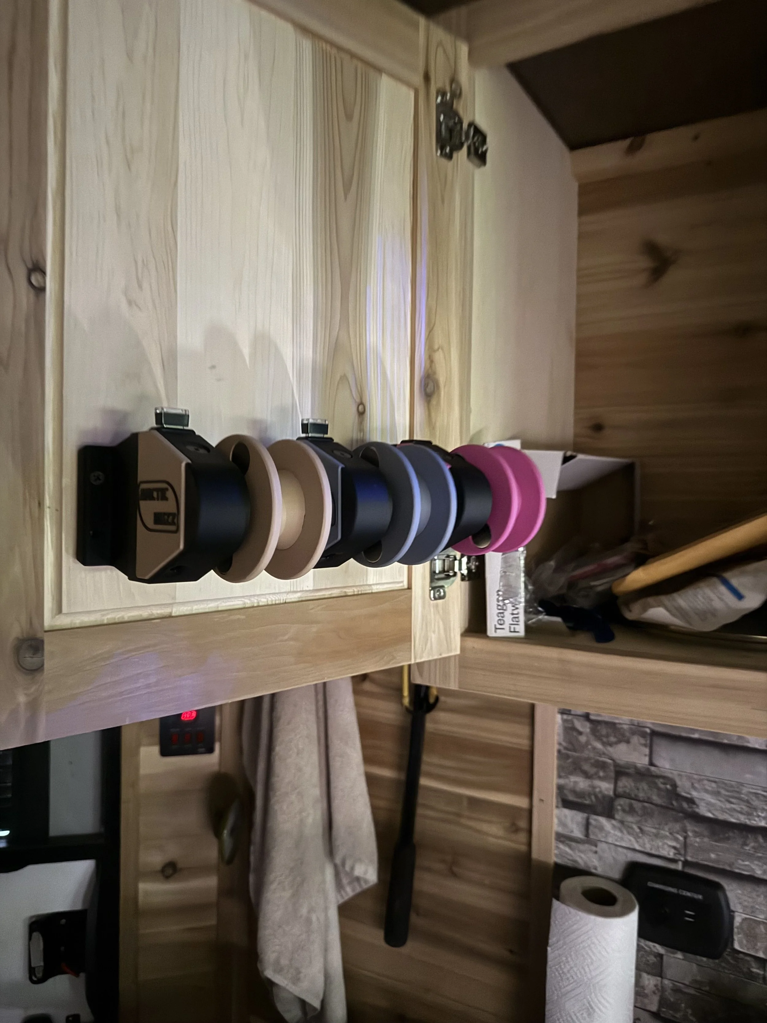 A wooden shelf holding several rolls of tape and a roll of paper towels, with a tissue box and a power strip visible underneath.