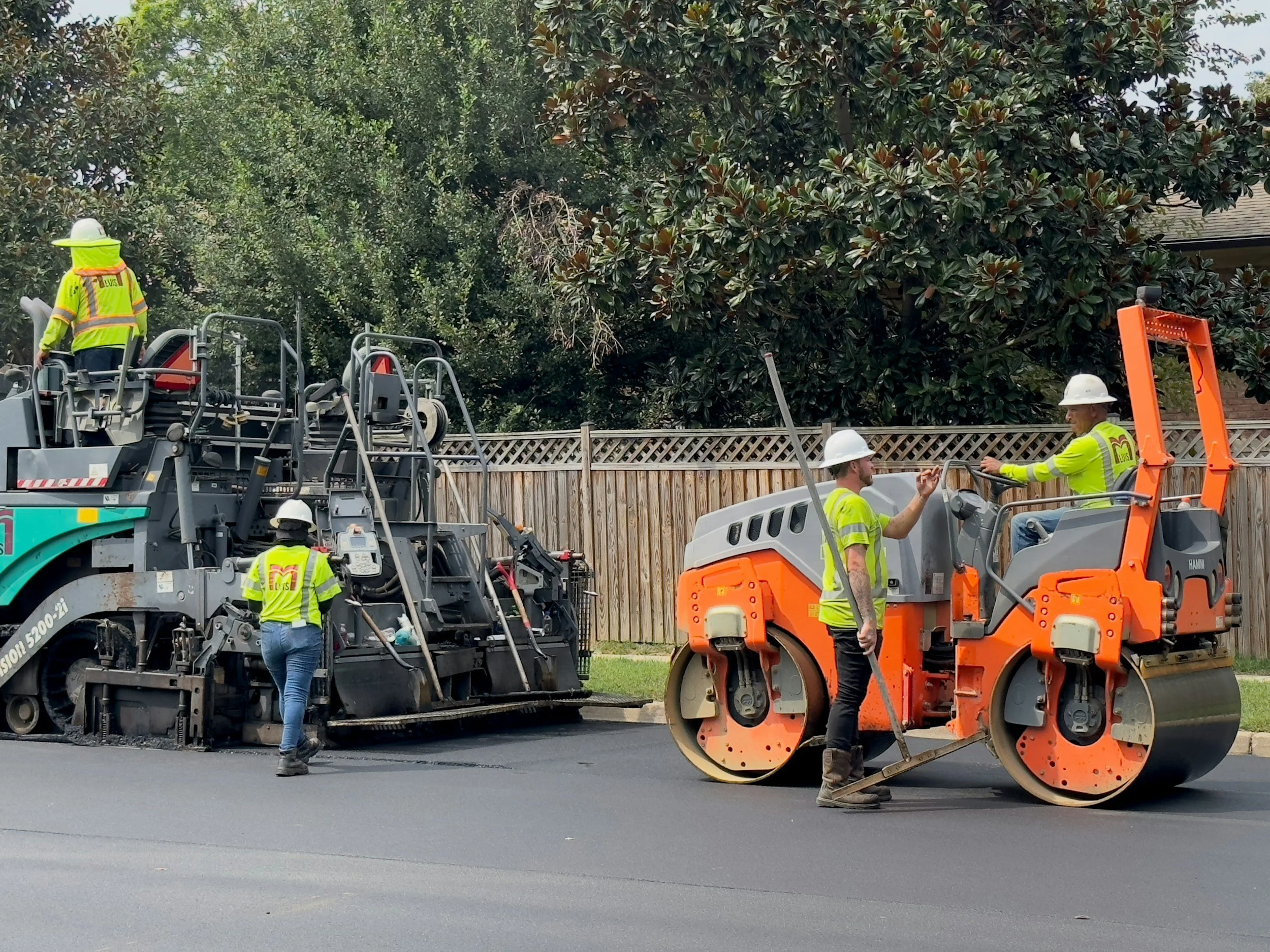 A professional asphalt paving crew operating heavy road construction equipment, representing the expert commercial paving and asphalt repair services offered by 7 County Sealcoating.