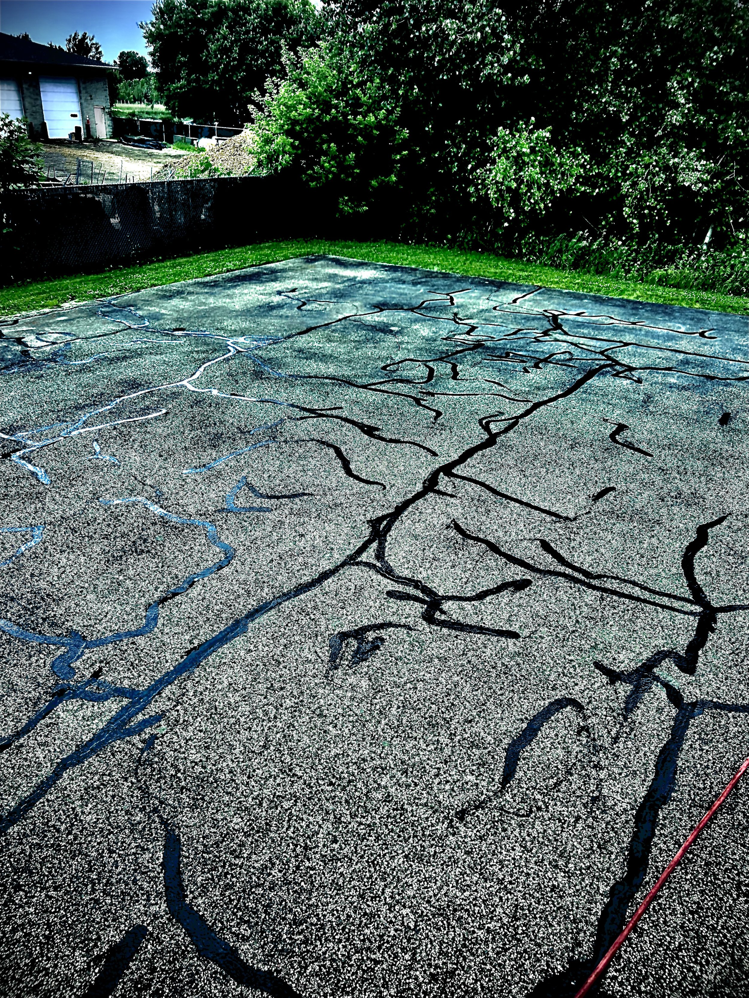 An edited photo highlighting extensive asphalt cleaning and professional crack filling services completed by 7 County Sealcoating at Revolt Electrical Services in Nowthen, Minnesota.