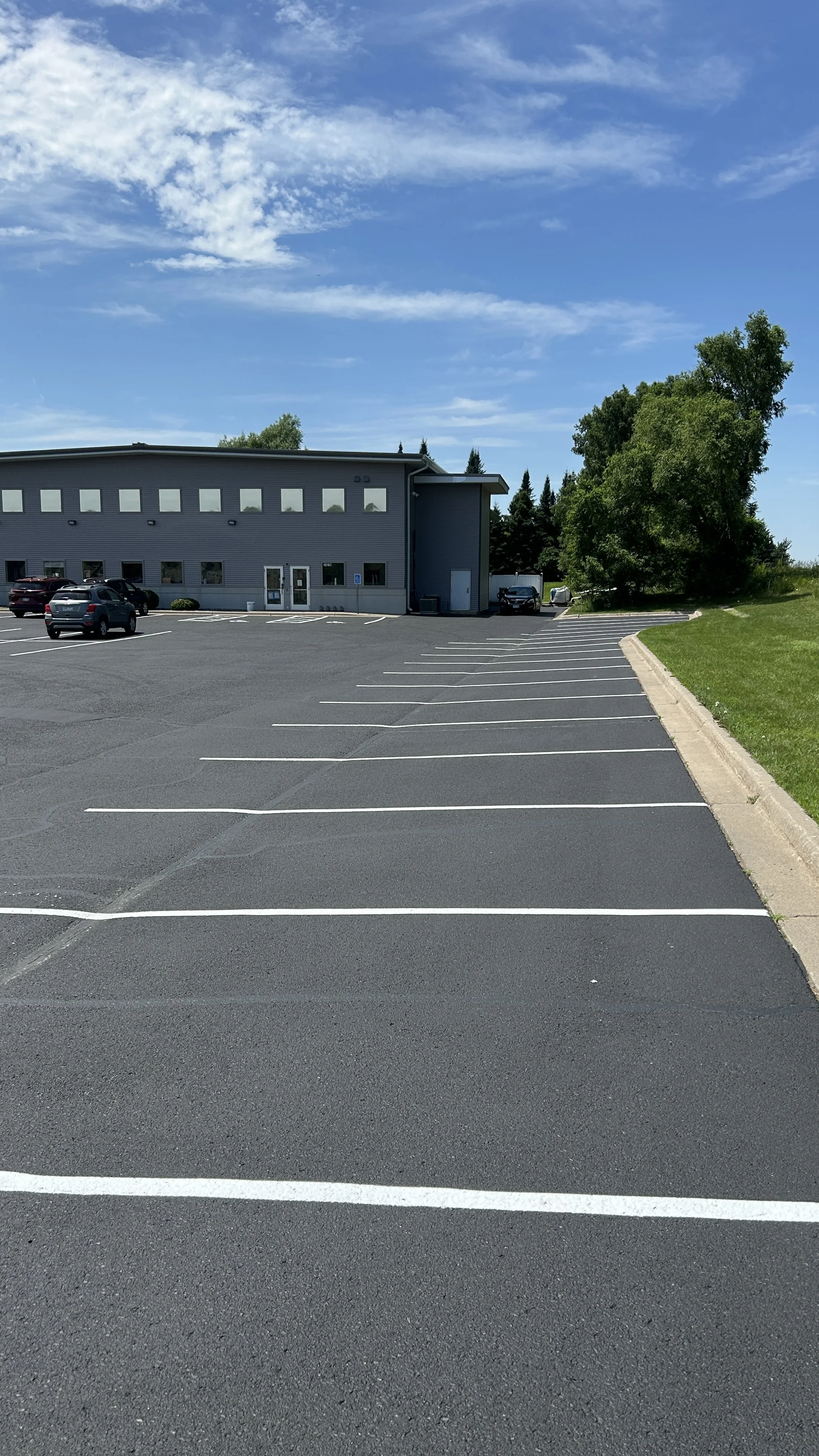 A freshly sealcoated commercial parking lot in Ham Lake, Minnesota, featuring precise white parking stall stripes and professionally protected asphalt provided by 7 County Sealcoating.
