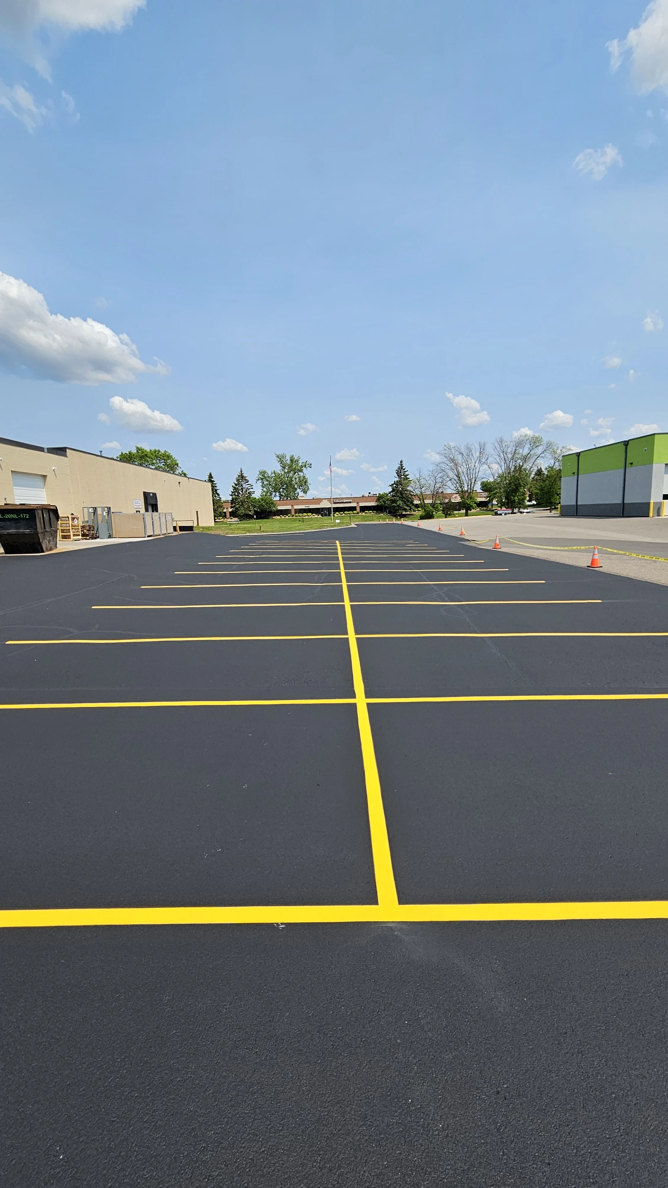 A freshly sealcoated commercial parking lot at AMP Manufacturing in Plymouth, Minnesota, featuring bright yellow line striping and expert asphalt patching by 7 County Sealcoating.