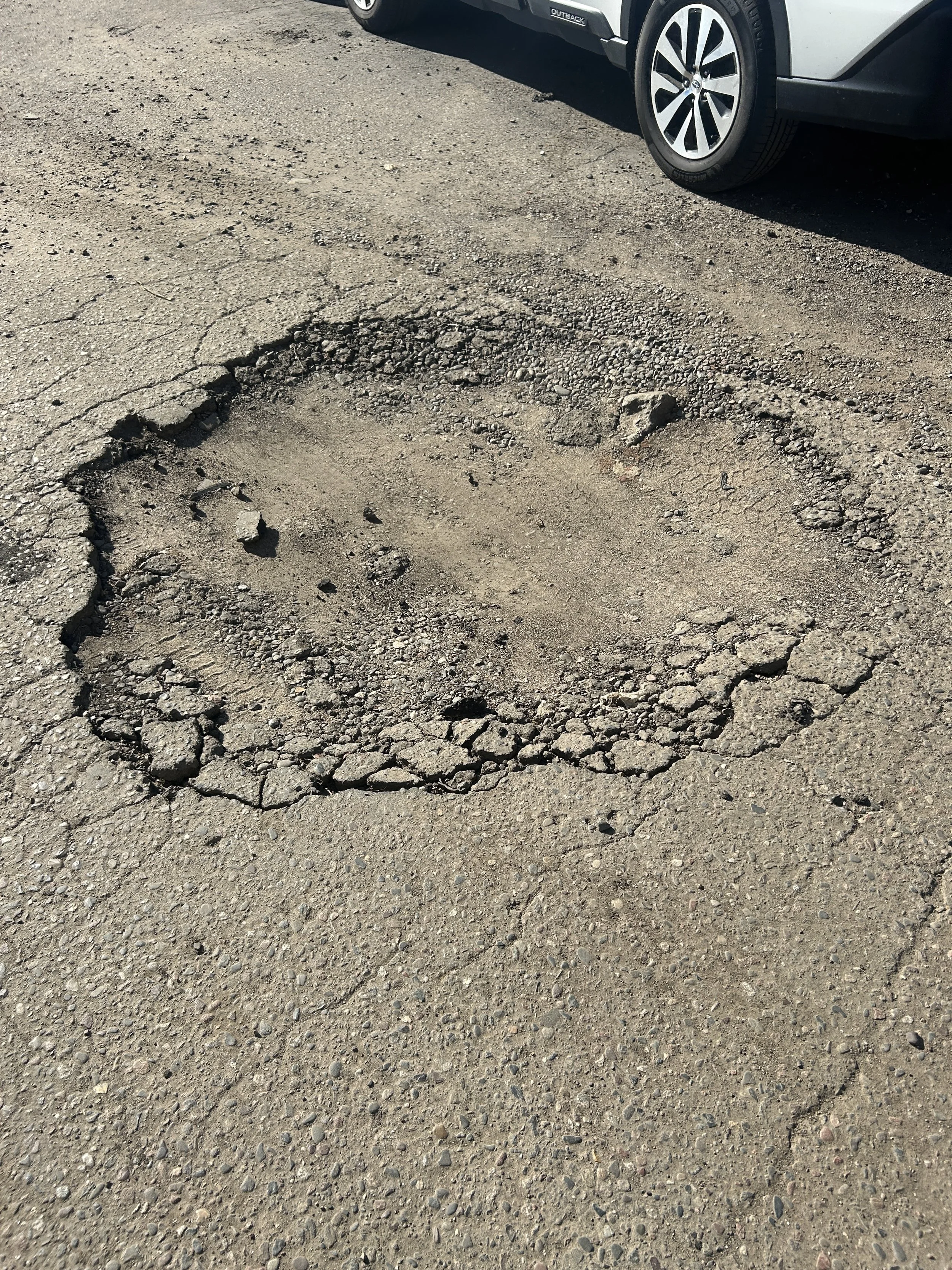 A severely damaged asphalt surface featuring a large pothole prior to being cleaned, prepped, and patched. Expert asphalt repair and patching services provided by 7 County Sealcoating at Sam's Autoworld in Fridley, Minnesota.