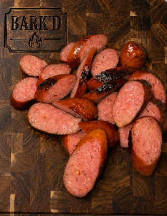 Sliced cooked sausages on a wooden cutting board, with a Bark'd branding card in the background.