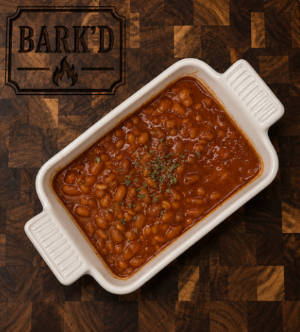 Baked beans in a white ceramic dish garnished with herbs, on a wooden surface with a Bark'd logo