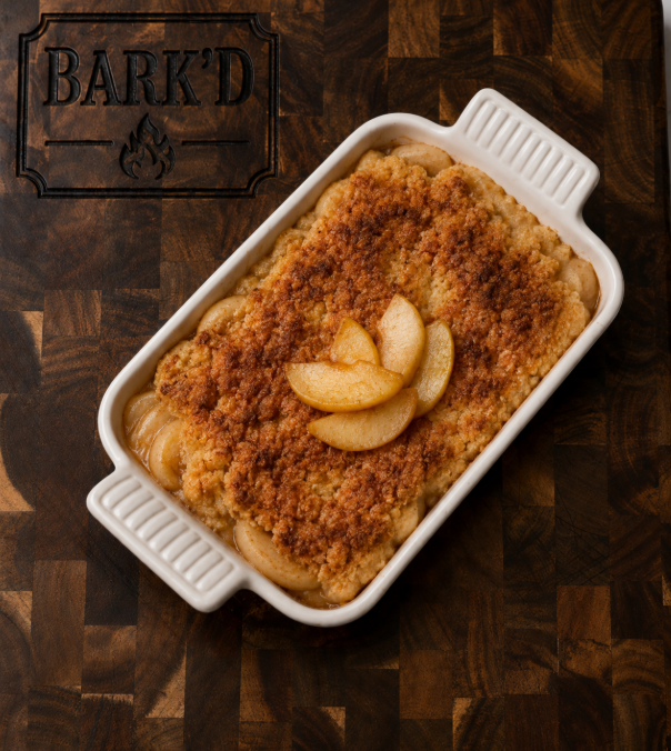 Baked fruit cobbler with slices of apple on top in a white baking dish on a wooden surface.