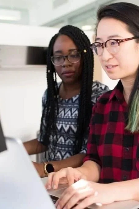 Two women working together at a computer in an office setting.