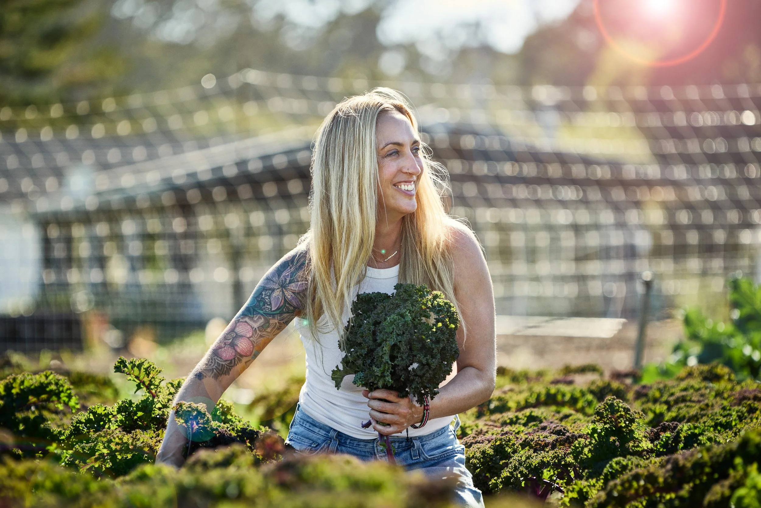 Debonair Events founder Rachel DiPaolo smiling while holding kale in a Bolinas farm with sunlight shining and trees in the background.