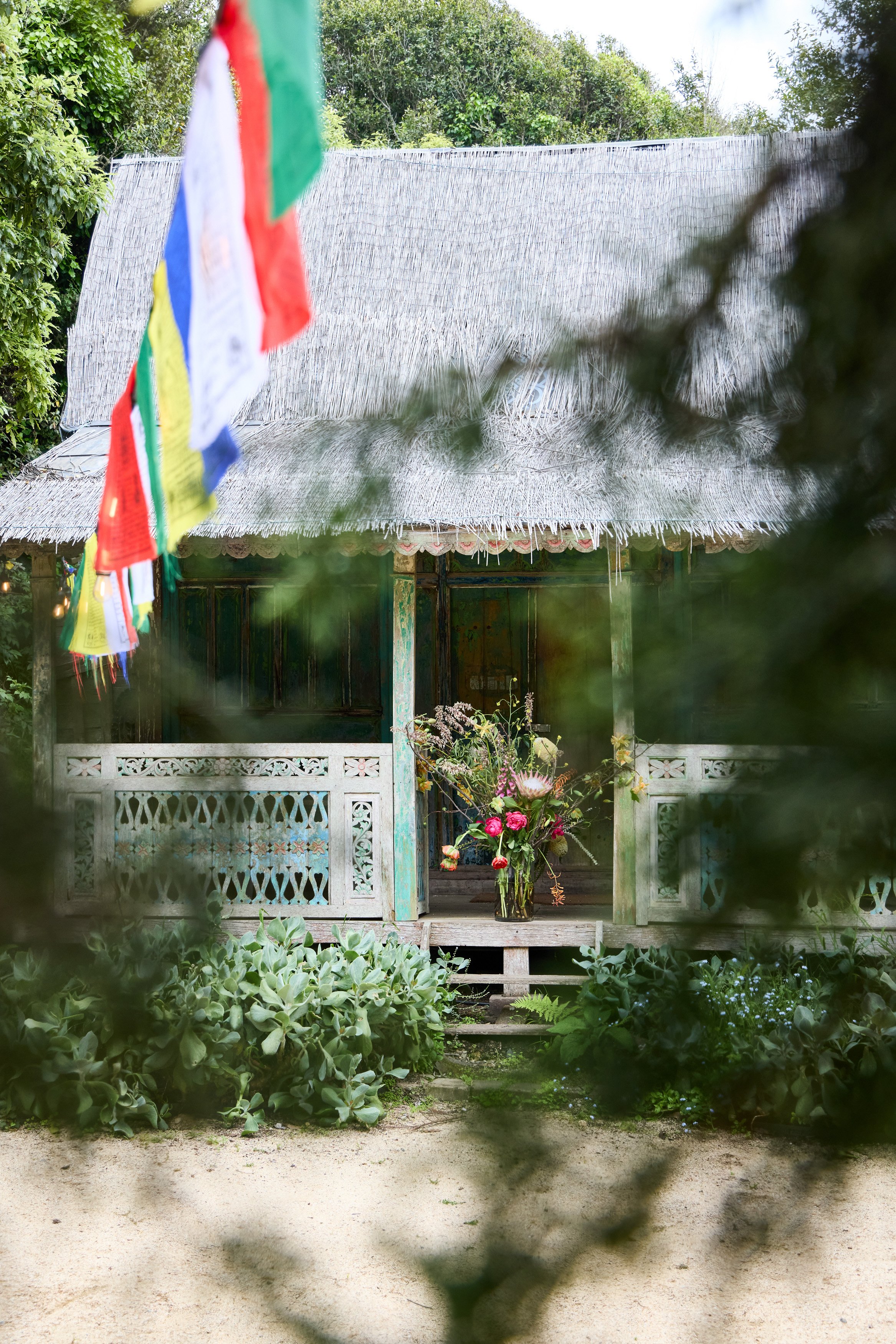 A rustic Stinson Beach wedding location with a bouquet of flowers in a vase, surrounded by greenery and prayer flags hanging nearby.
