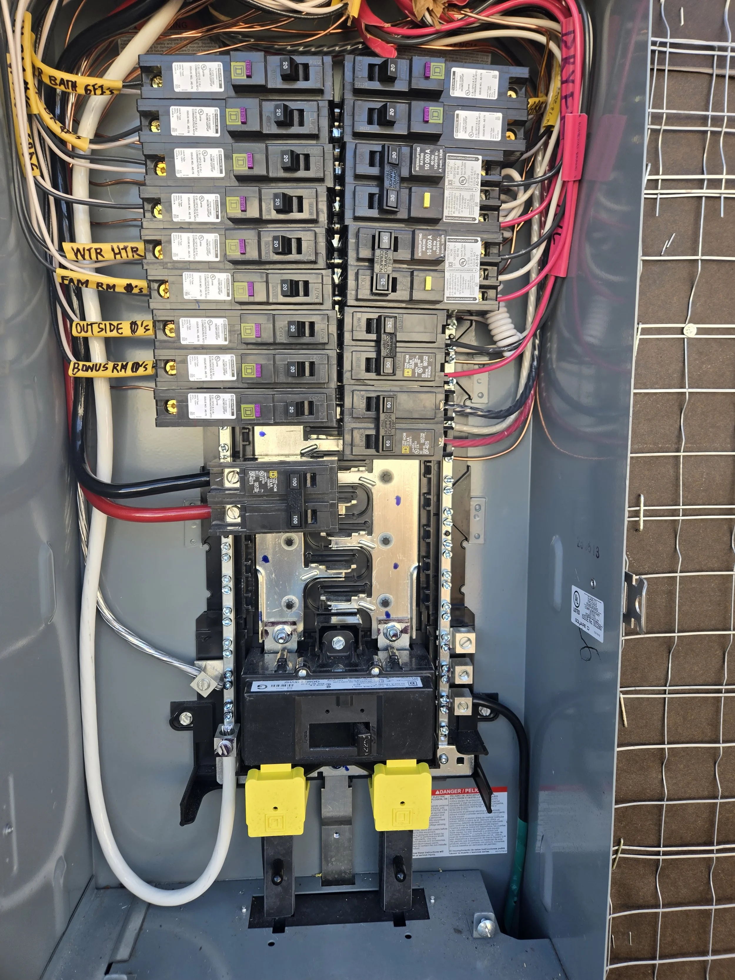 An electrical breaker panel with multiple circuit breakers labeled for different areas such as 'WIR HTR', 'FAN RM', and 'OUTSIDE' with wires connected to each breaker.