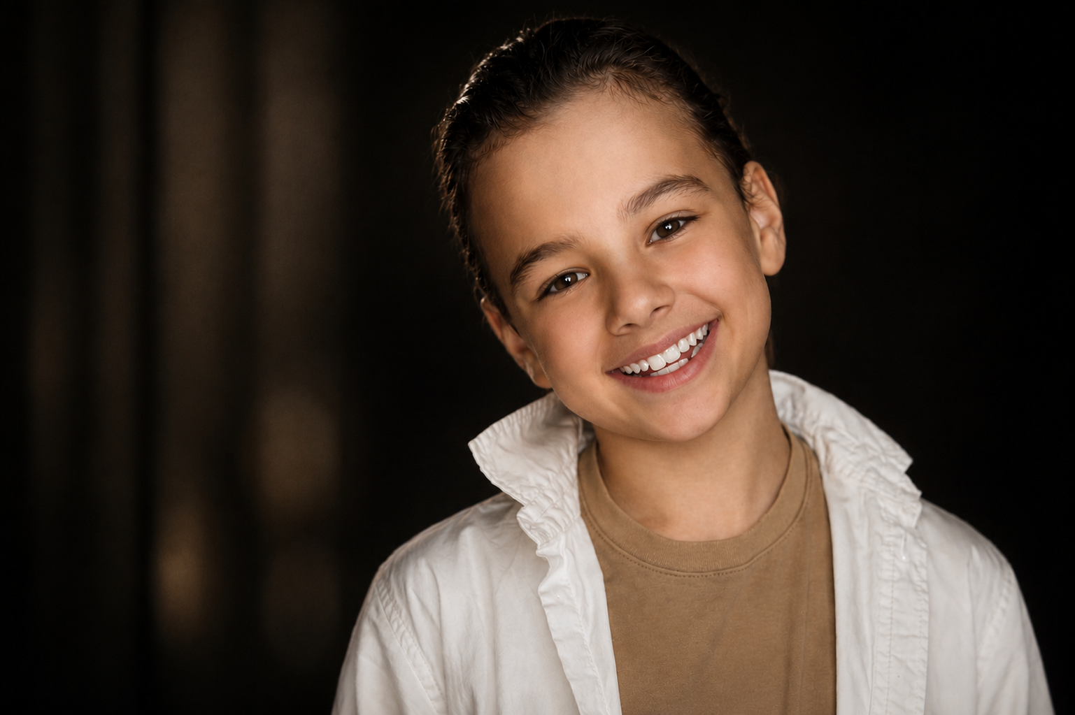 Portrait of a smiling young girl with short dark hair, wearing a beige t-shirt and a white shirt.