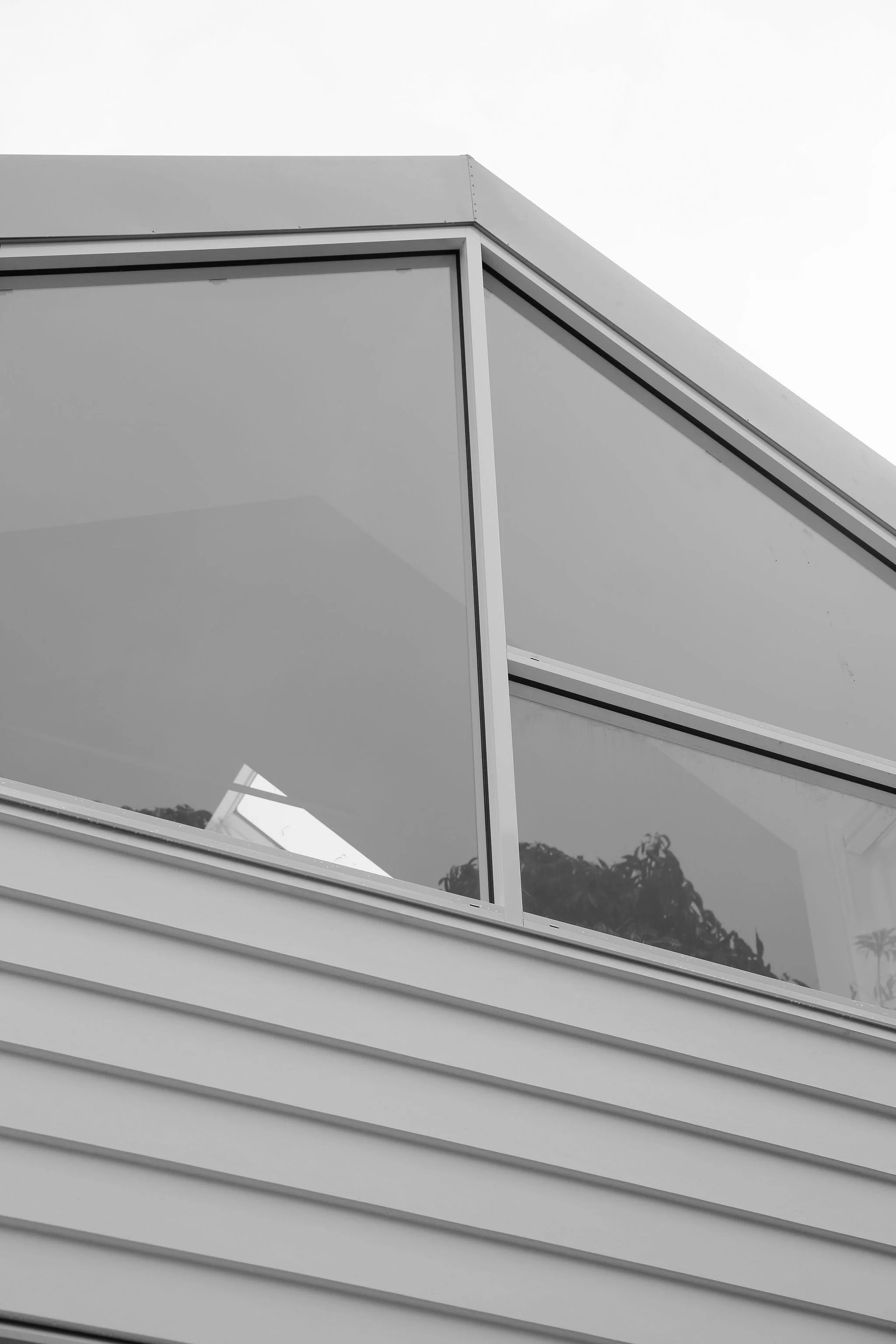 Modern building with large glass windows and horizontal siding, seen from an upward angle, with a clear sky in the background.