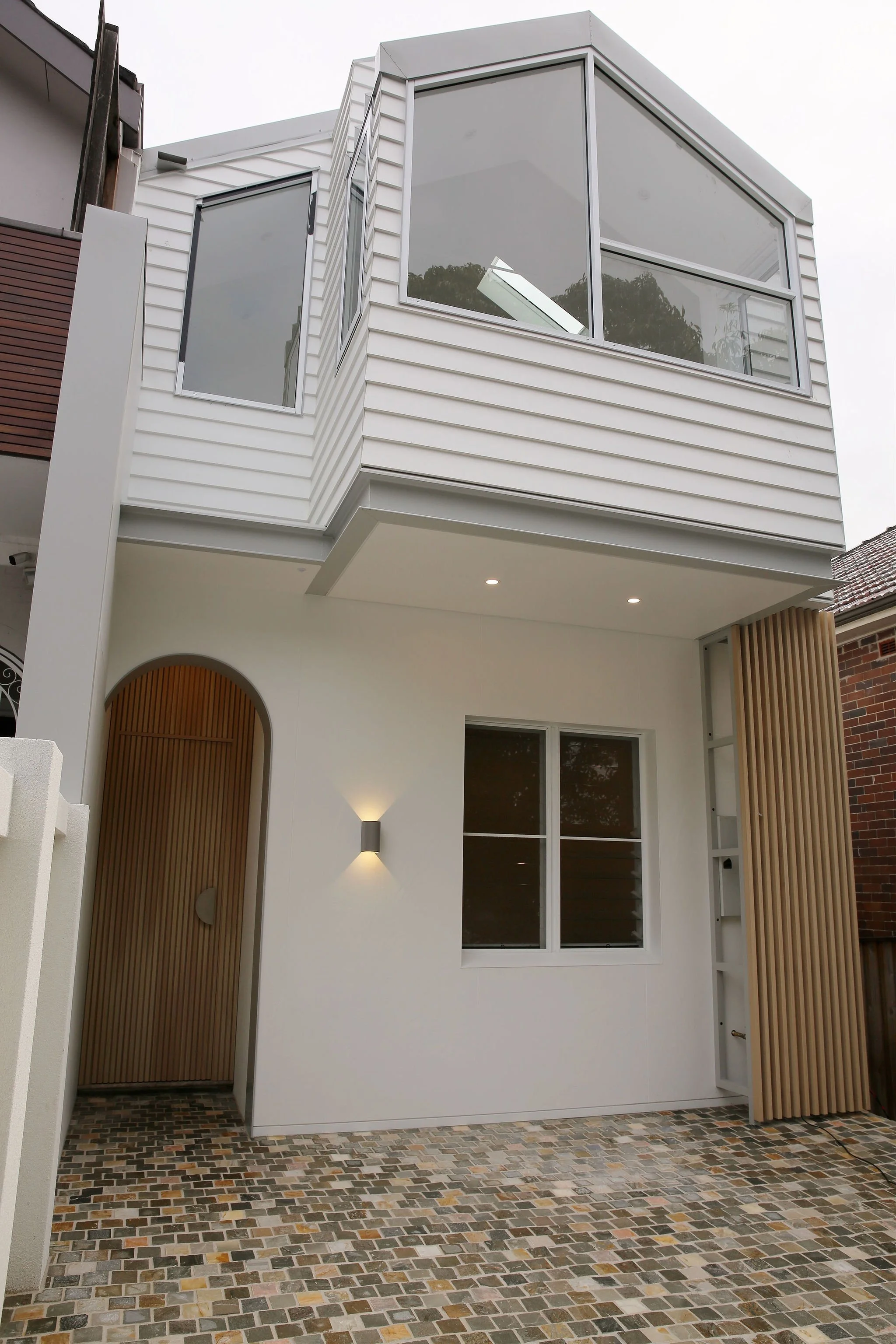 Modern white residential building with large windows, wooden accents, and a tiled front porch area.