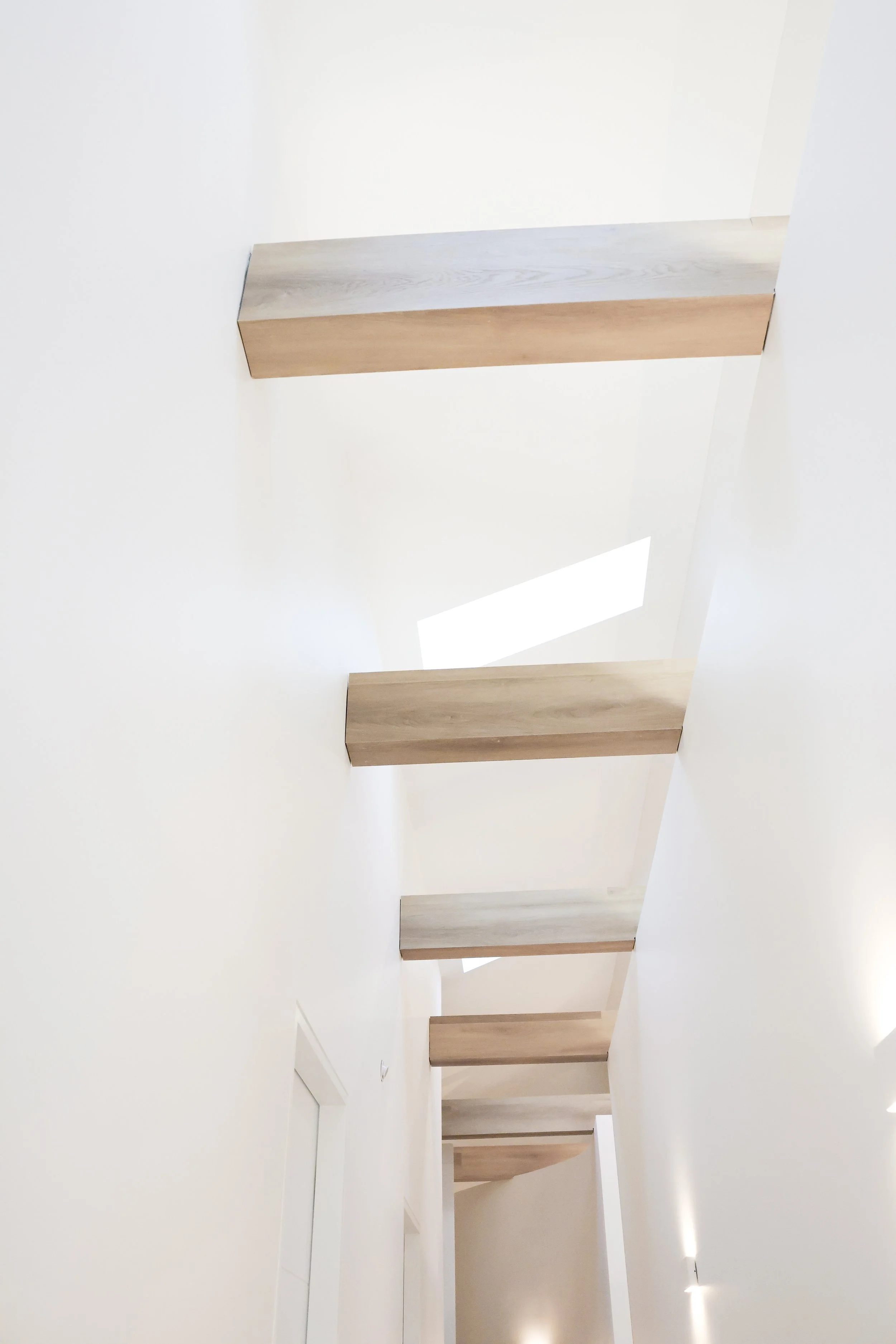Multiple wooden stair treads mounted on white walls, viewed from below with upward perspective.