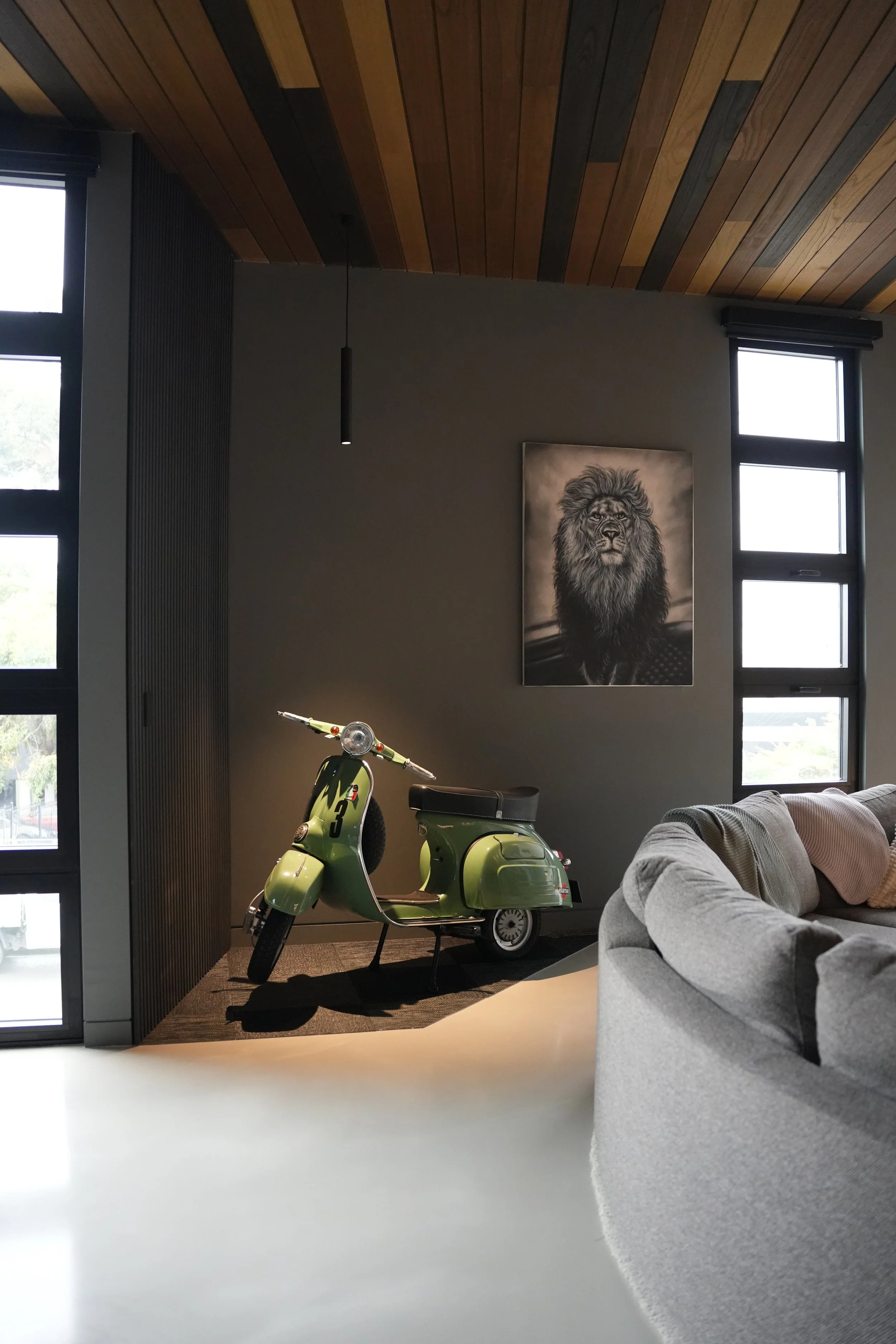 Living room with a lime green vintage scooter, modern decor, a large lion portrait on the wall, and gray furniture near large windows with natural light.