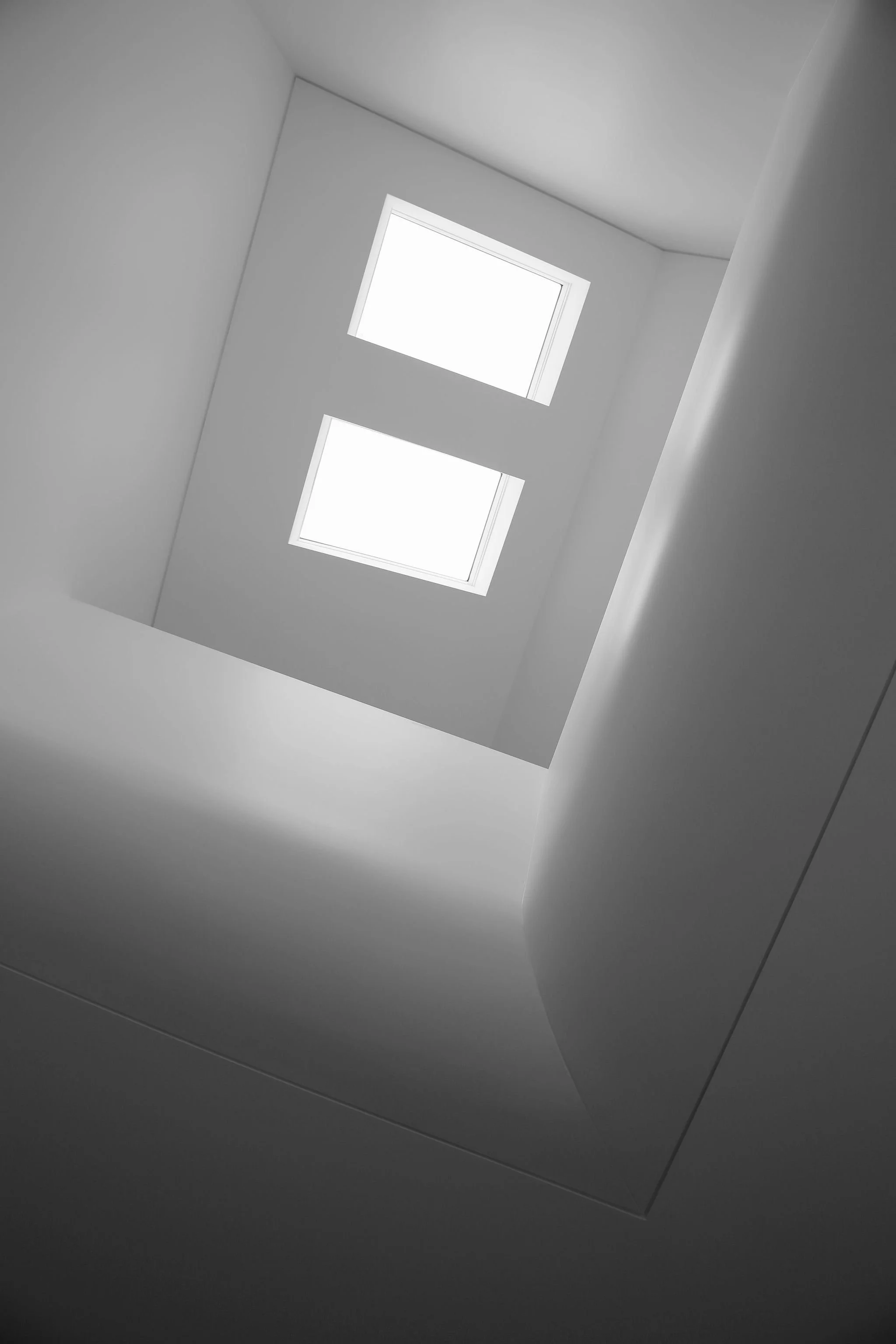 Looking up at two rectangular skylights in a white ceiling, with shadows cast on the surrounding surfaces.