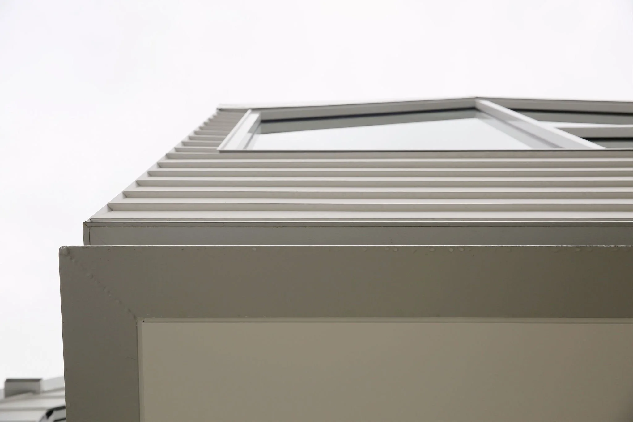 A modern building with white exterior walls and horizontal lines, viewed from below against a cloudy sky.