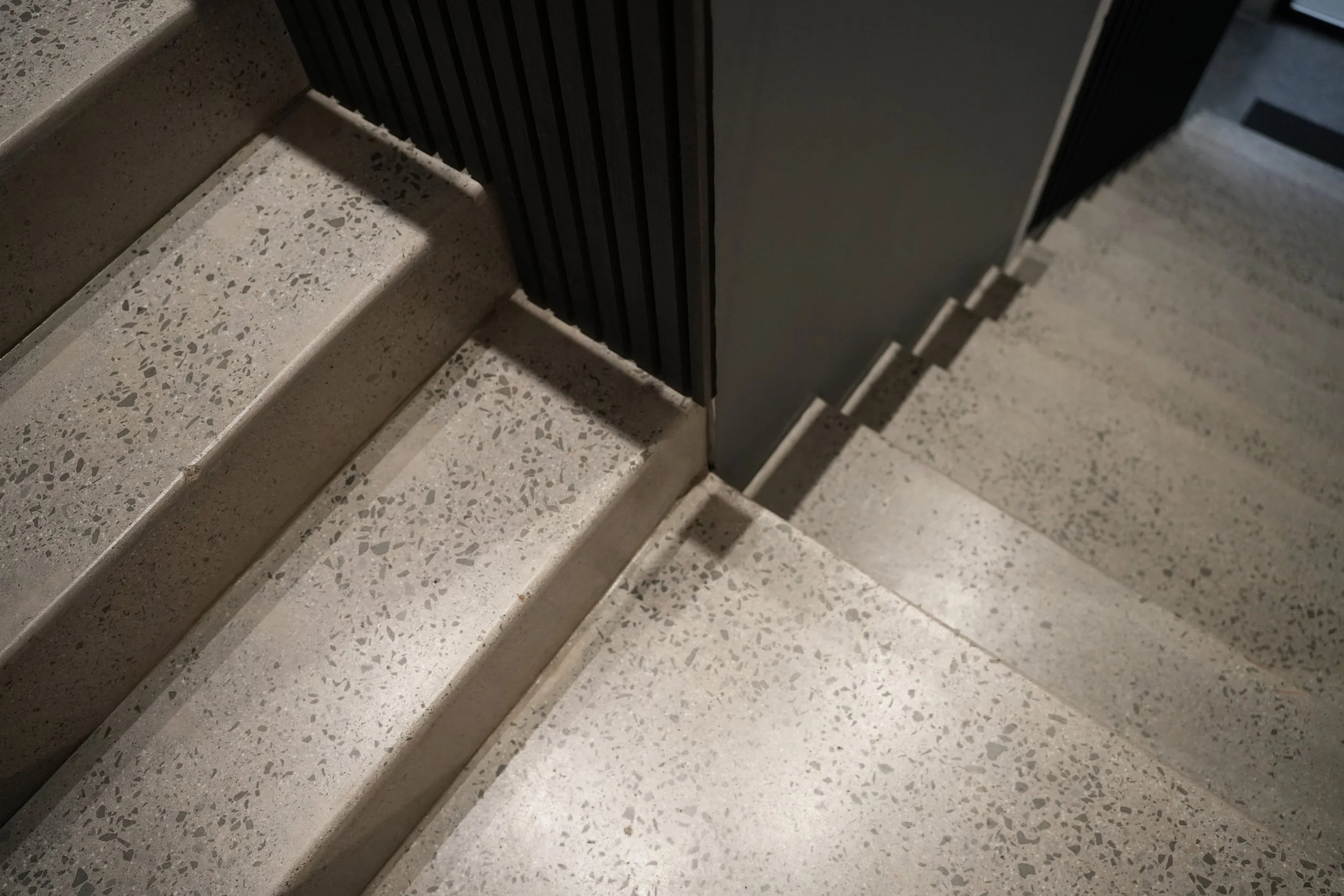 Close-up view of terrazzo stairs and the bottom edge of a black door with vertical ridges.
