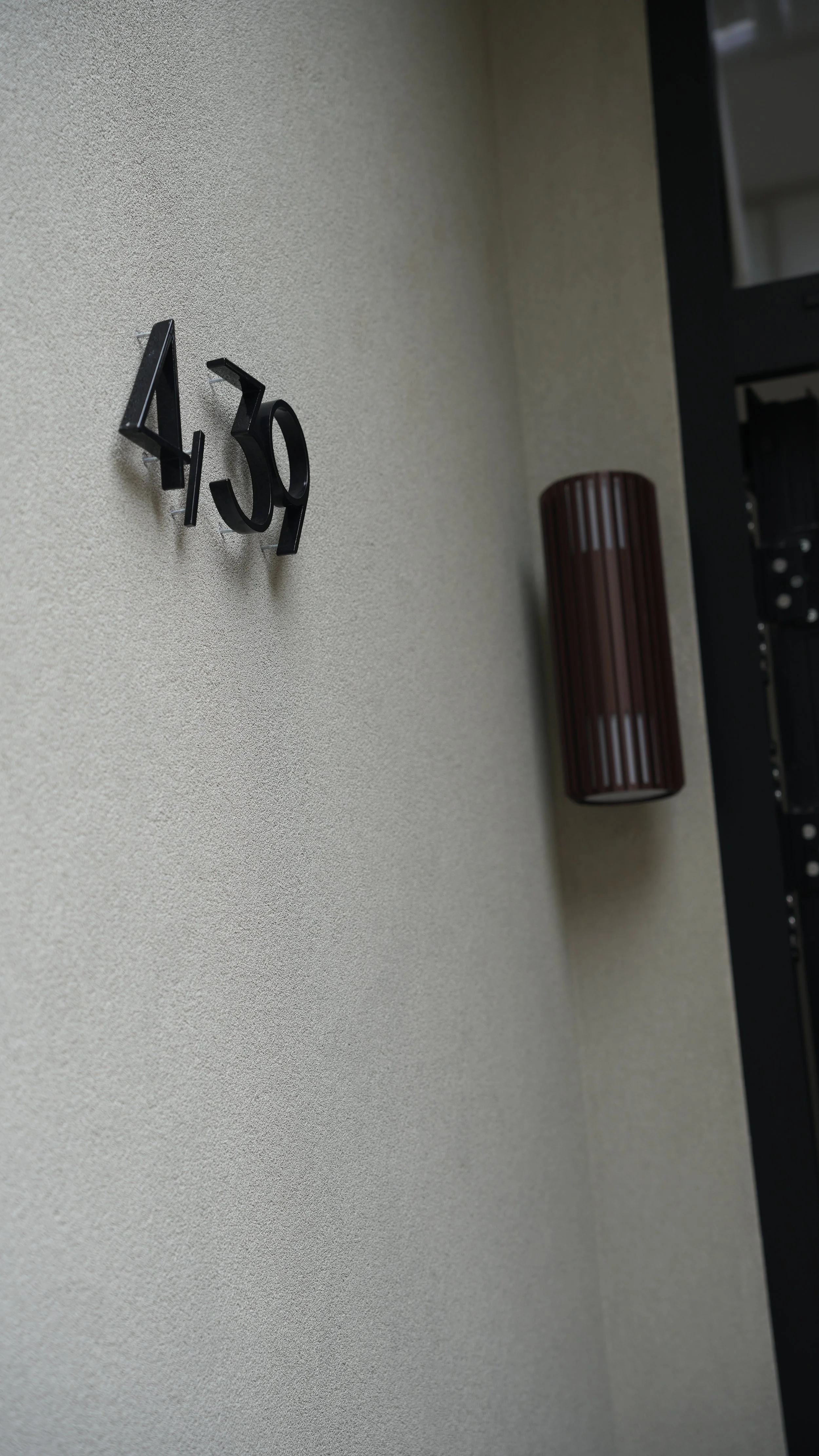 Close-up of the number 430 on a textured beige wall, with a dark brown cylindrical wall sconce to the right.