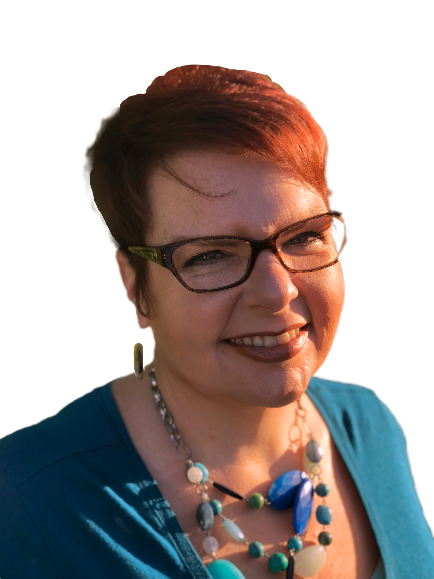 A close-up of a woman with short reddish-brown hair, wearing glasses, a turquoise top, and colorful jewelry, smiling outdoors in warm sunlight.