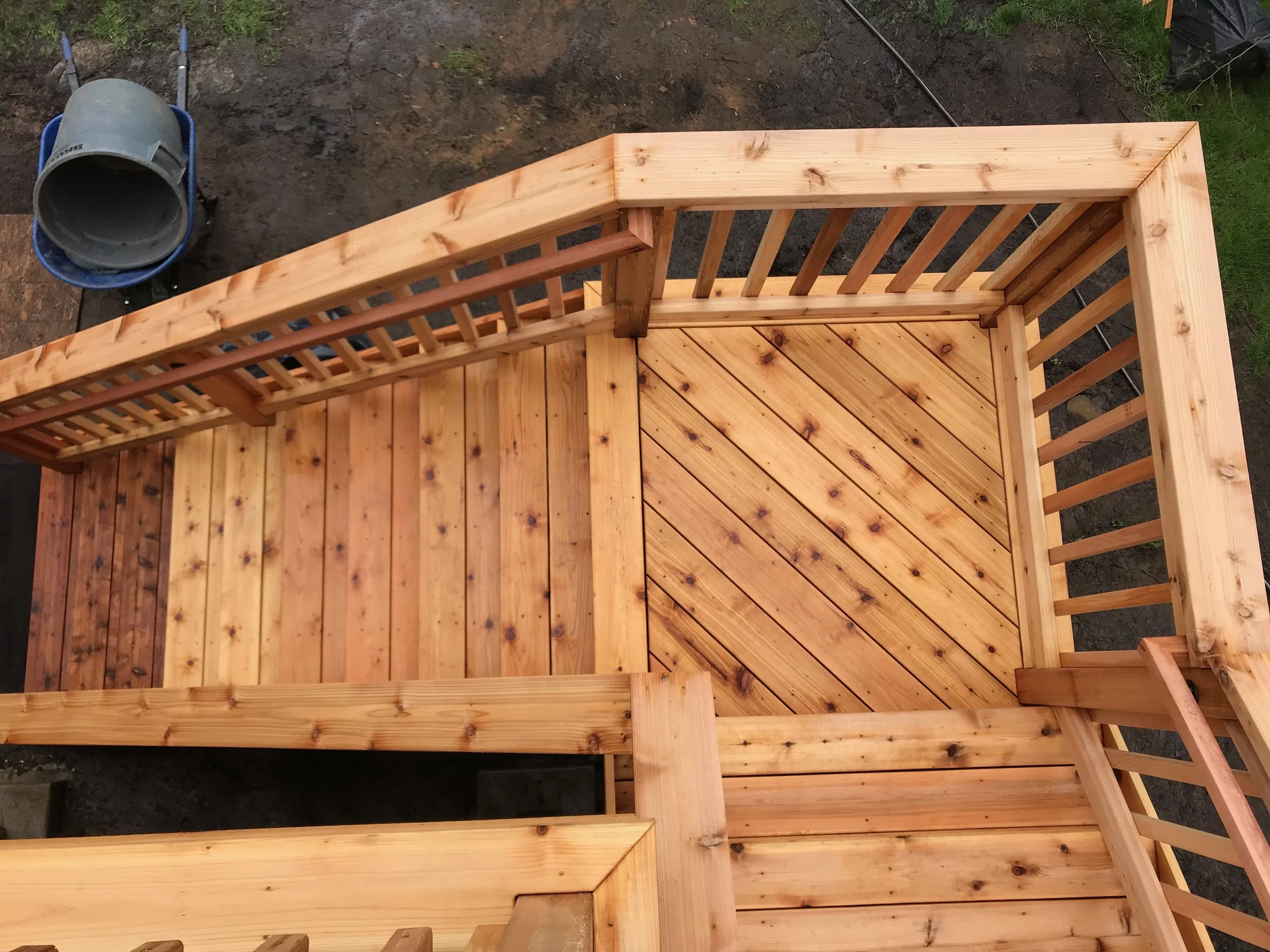 The photo shows a wooden staircase under construction outdoors, with a concrete mixer and a tilting wheelbarrow nearby.