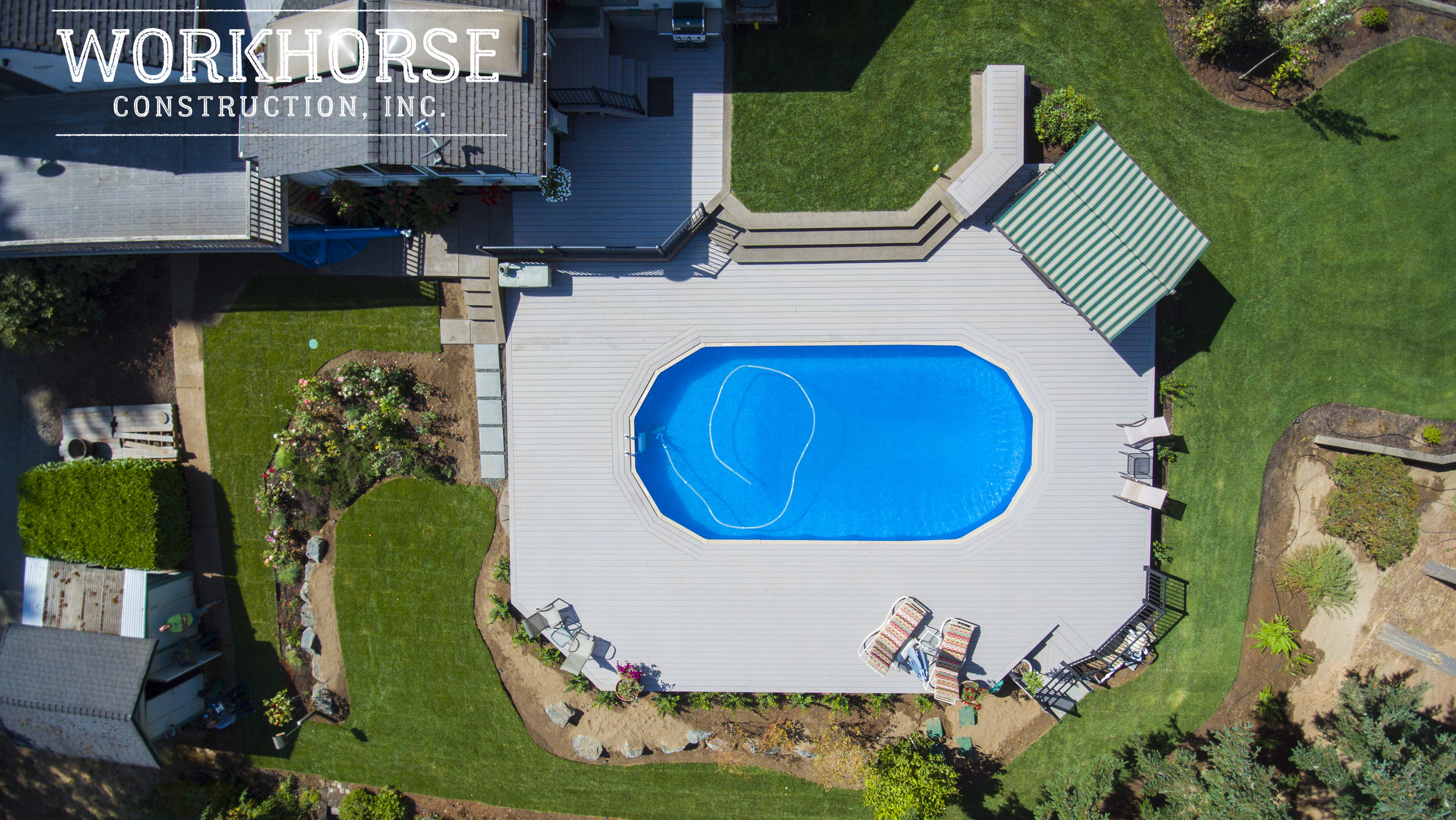 Aerial view of a backyard with a swimming pool, multi-level decks, green lawns, flower beds, and outdoor furniture.