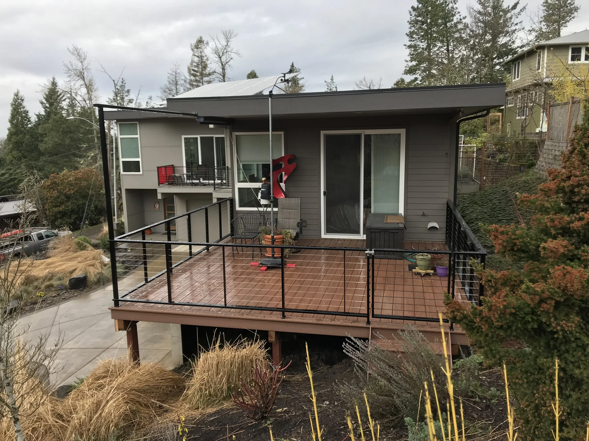 Backyard deck with patio furniture, potted plants, and a red slide, overlooking neighboring houses and trees under cloudy sky.
