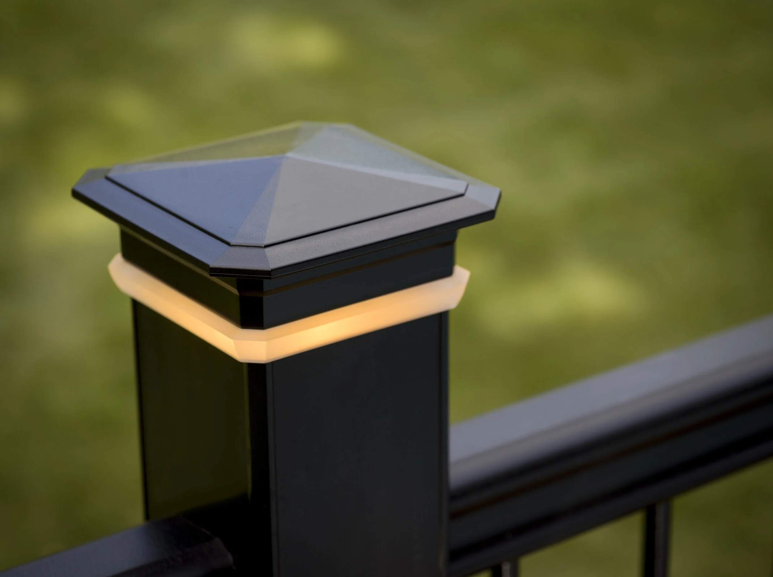 Close-up of a modern outdoor post light fixture on a black pole with a blurred green background.