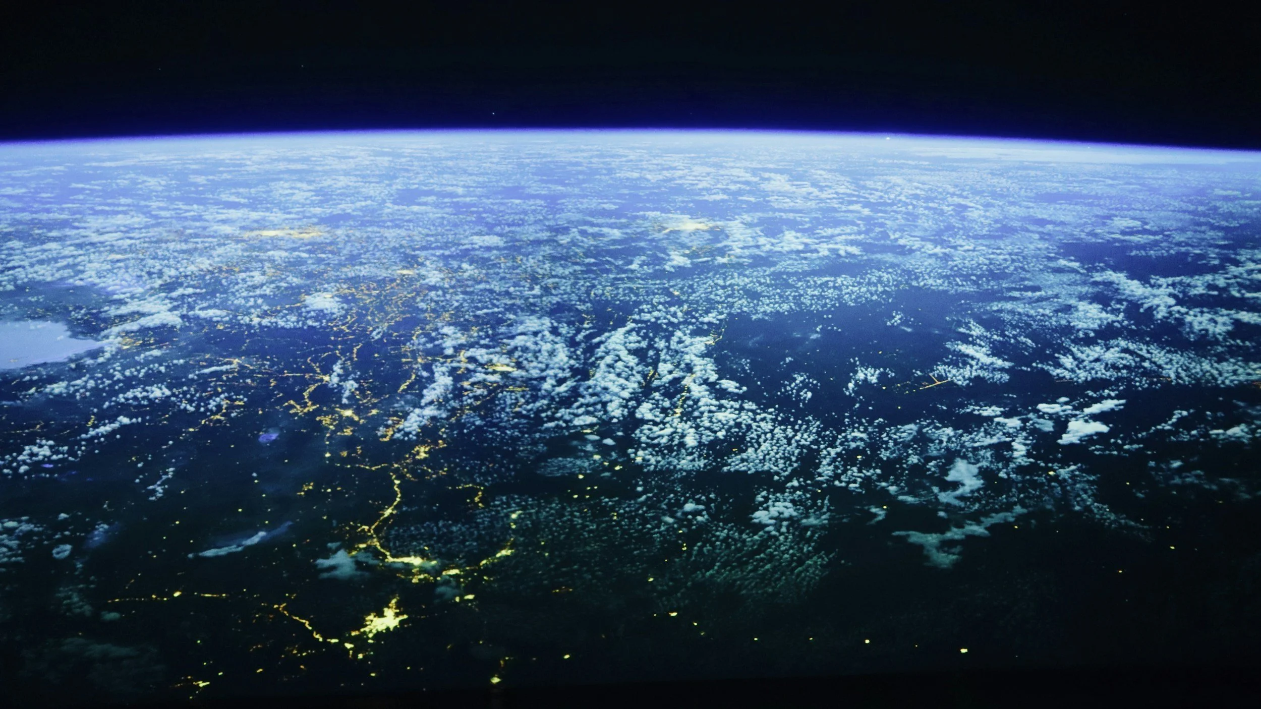 View of Earth's horizon at night from space, showing illuminated cities and cloud cover.