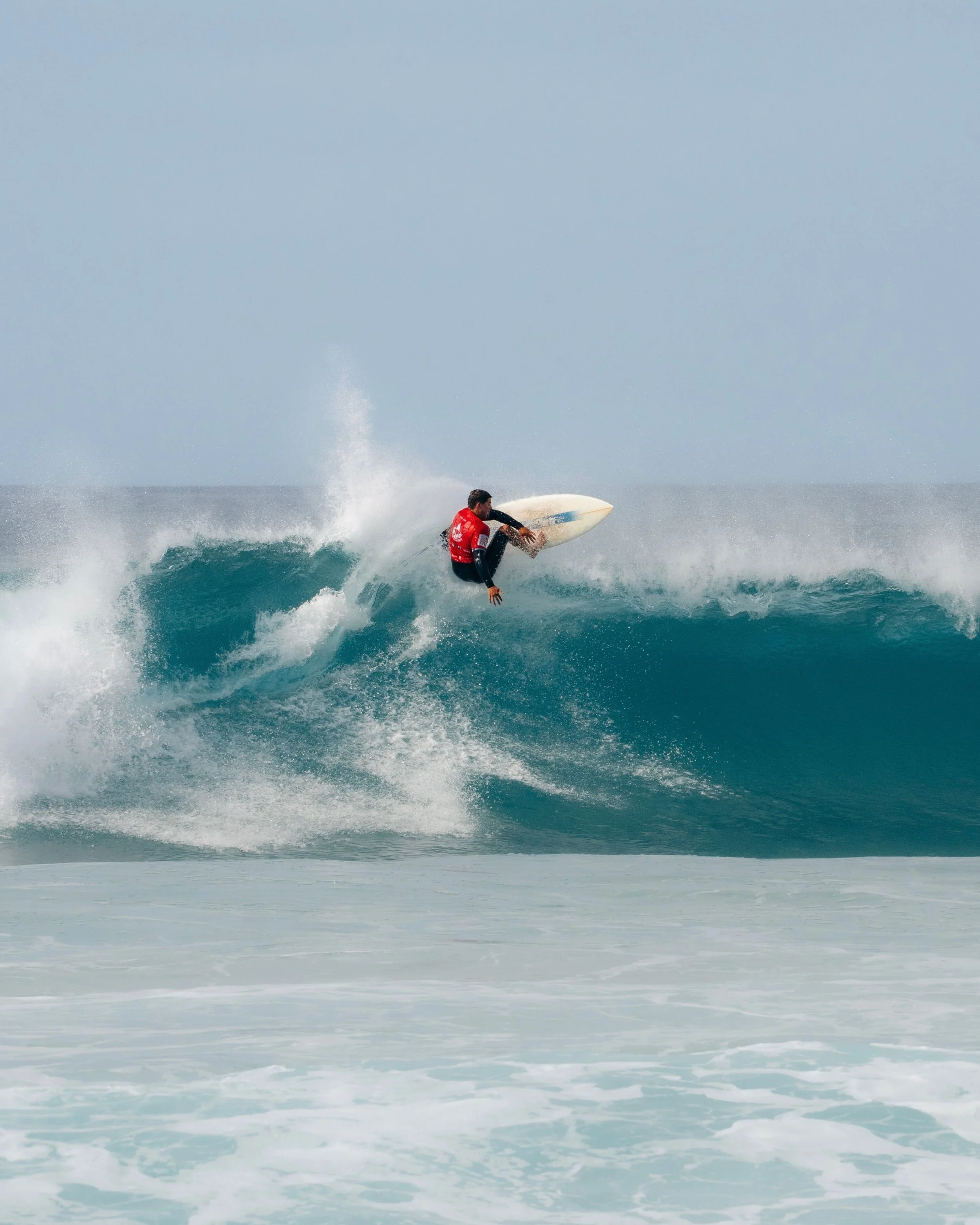 A surfer in a red wetsuit riding a wave on a sunny day.